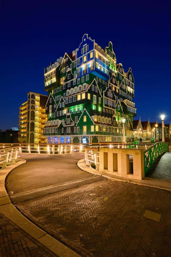 Hotel 桌布 壁紙 — 一座引人注目的綠色和白色荷蘭風格建築，在深藍色天空的襯托下，夜晚被溫暖的燈光照亮。