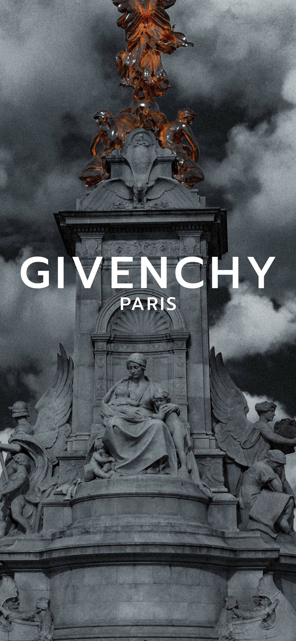 Givenchy 桌布 壁紙 — 一座戲劇性的單色紀念碑，飾有華麗的雕塑，頂部有一個熾熱的金色天使形象，背景是暴風雨雲。