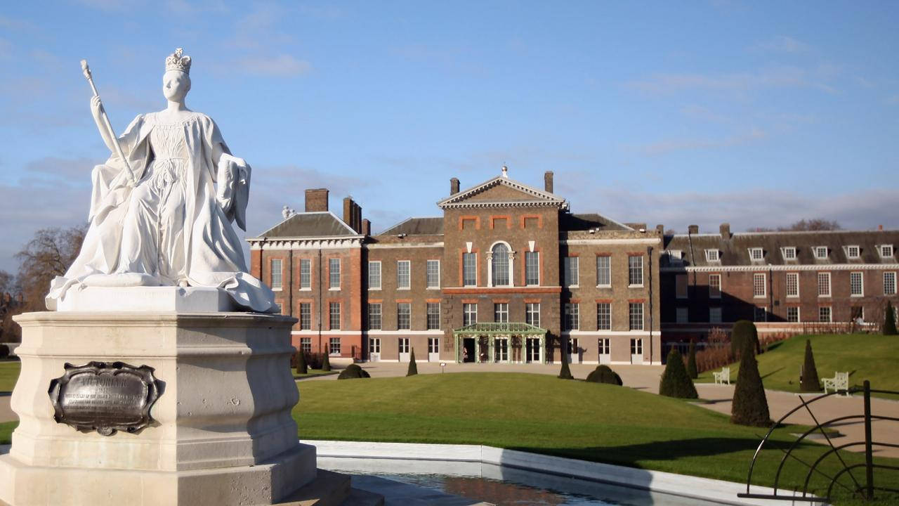 England 桌布 壁紙 — 一座戴著王冠、手持權杖的白色女王雕像矗立在晴朗藍天下的一座莊嚴磚造莊園前。