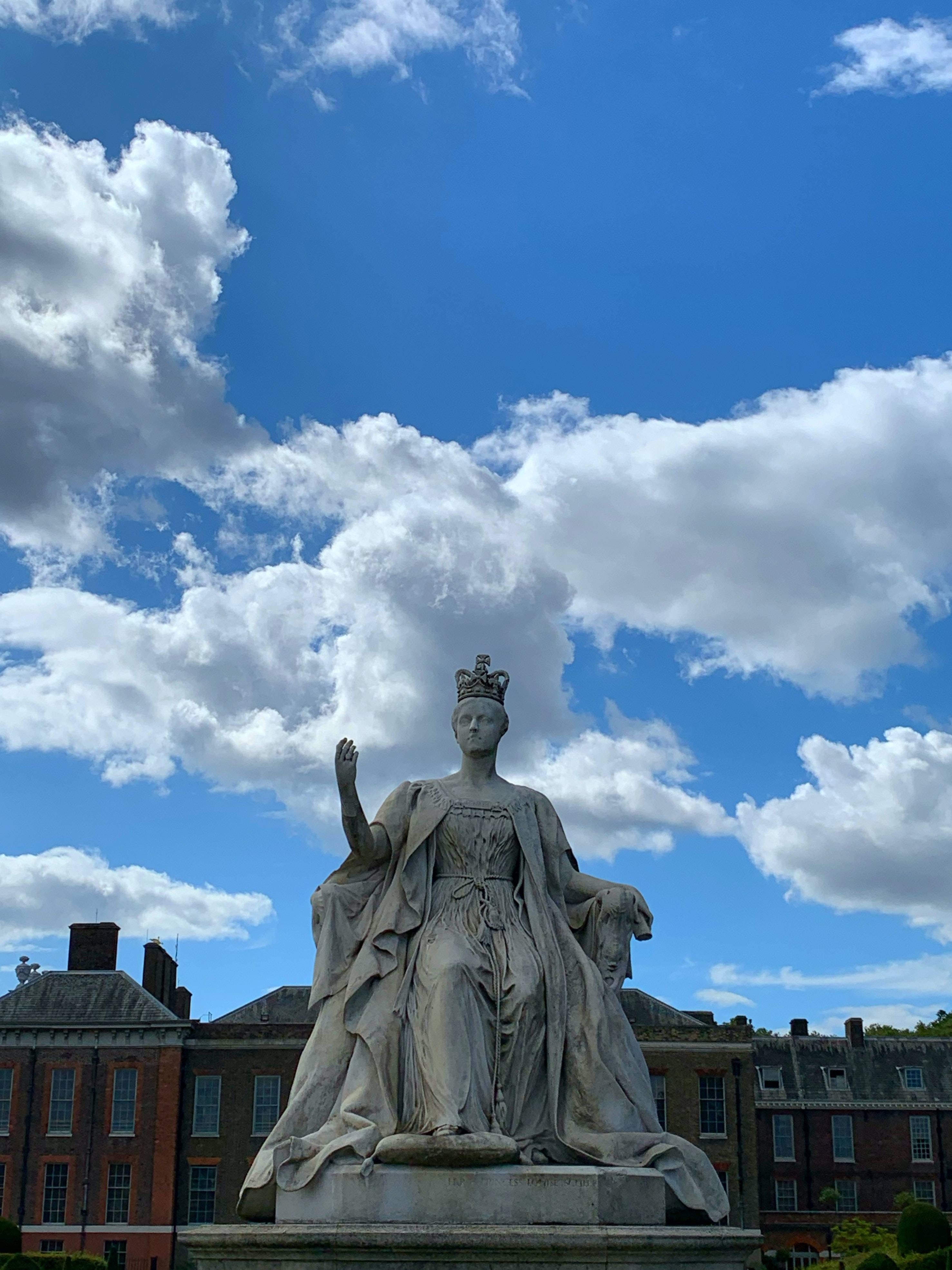 England 桌布 壁紙 — 一座戴著王冠的女王雄偉石像，在充滿蓬鬆白雲的鮮豔藍天下威嚴地矗立。