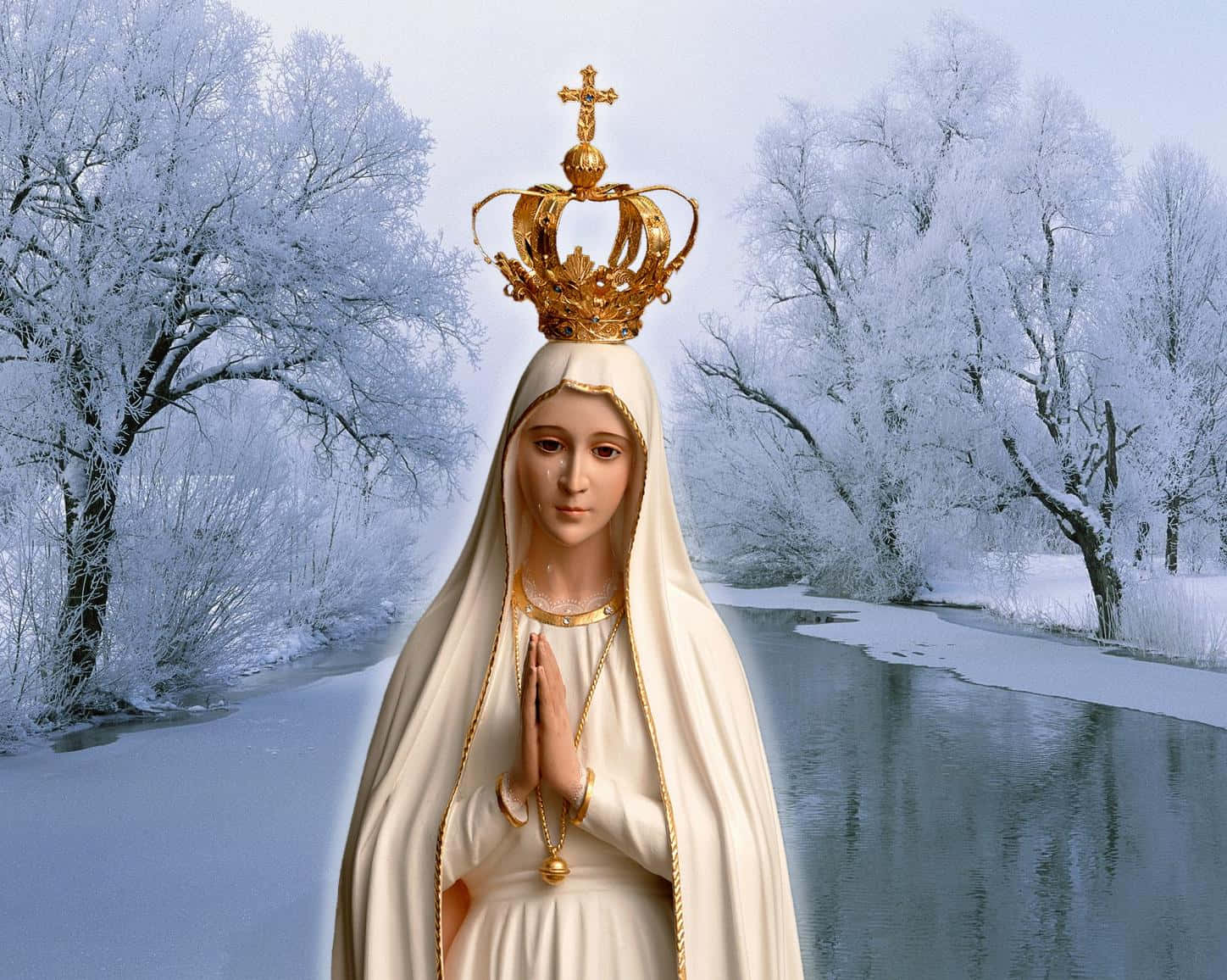 Mother Mary 桌布 壁紙 — 一座戴著白色面紗和金色皇冠的聖母瑪利亞寧靜雕像，矗立在結冰河流旁的雪地冬季景觀中。