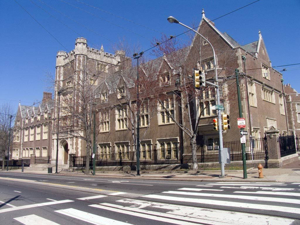 美學 桌布 壁紙 — 一座擁有哥德式建築風格的大型歷史磚造建築，在晴朗的藍天下，矗立在一條設有斑馬線和交通號誌的繁忙街道旁。