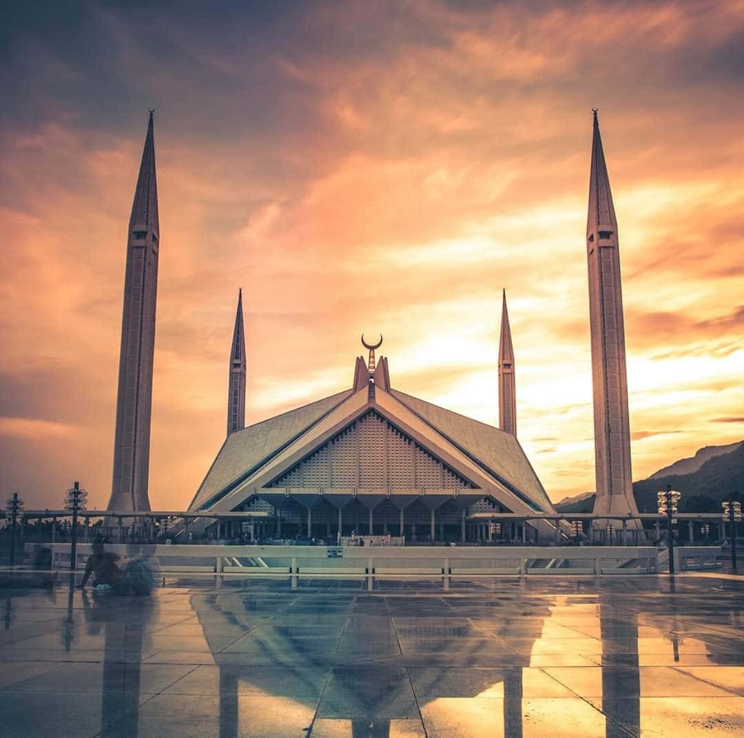 Pakistan 桌布 壁紙 — 一座擁有四座高聳宣禮塔的宏偉清真寺，在火紅的日落天空下，美麗地倒映在濕漉漉的路面上。