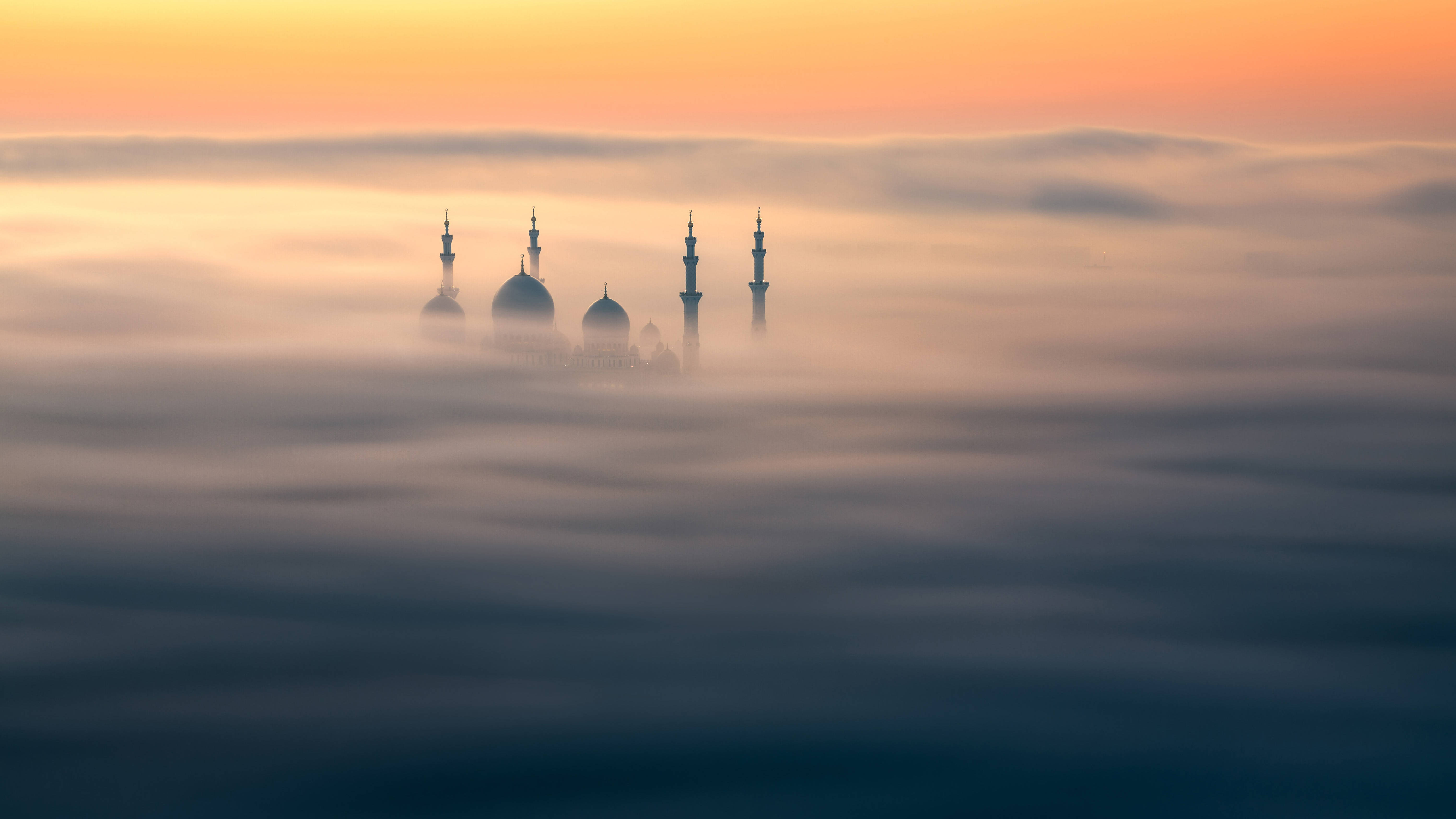 Arab 桌布 壁紙 — 一座擁有圓頂和宣禮塔的清真寺在日出時分，在溫暖的橙色天空下，寧靜地聳立於霧海之上。