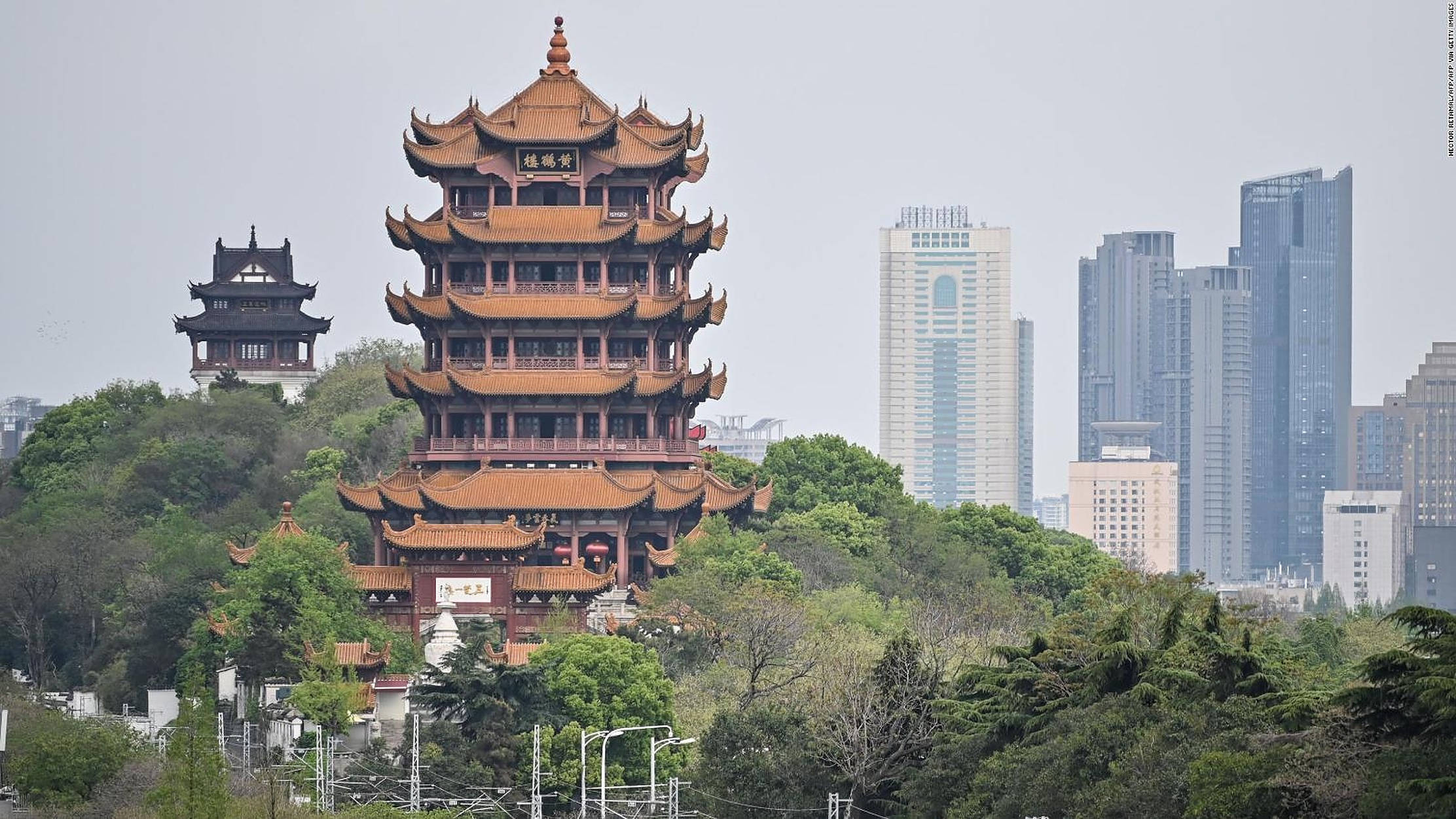 Wuhan 桌布 壁紙 — 一座擁有橙色屋頂的傳統中式寶塔矗立在鬱鬱蔥蔥的綠色山丘上，被現代摩天大樓環繞，天空多雲。