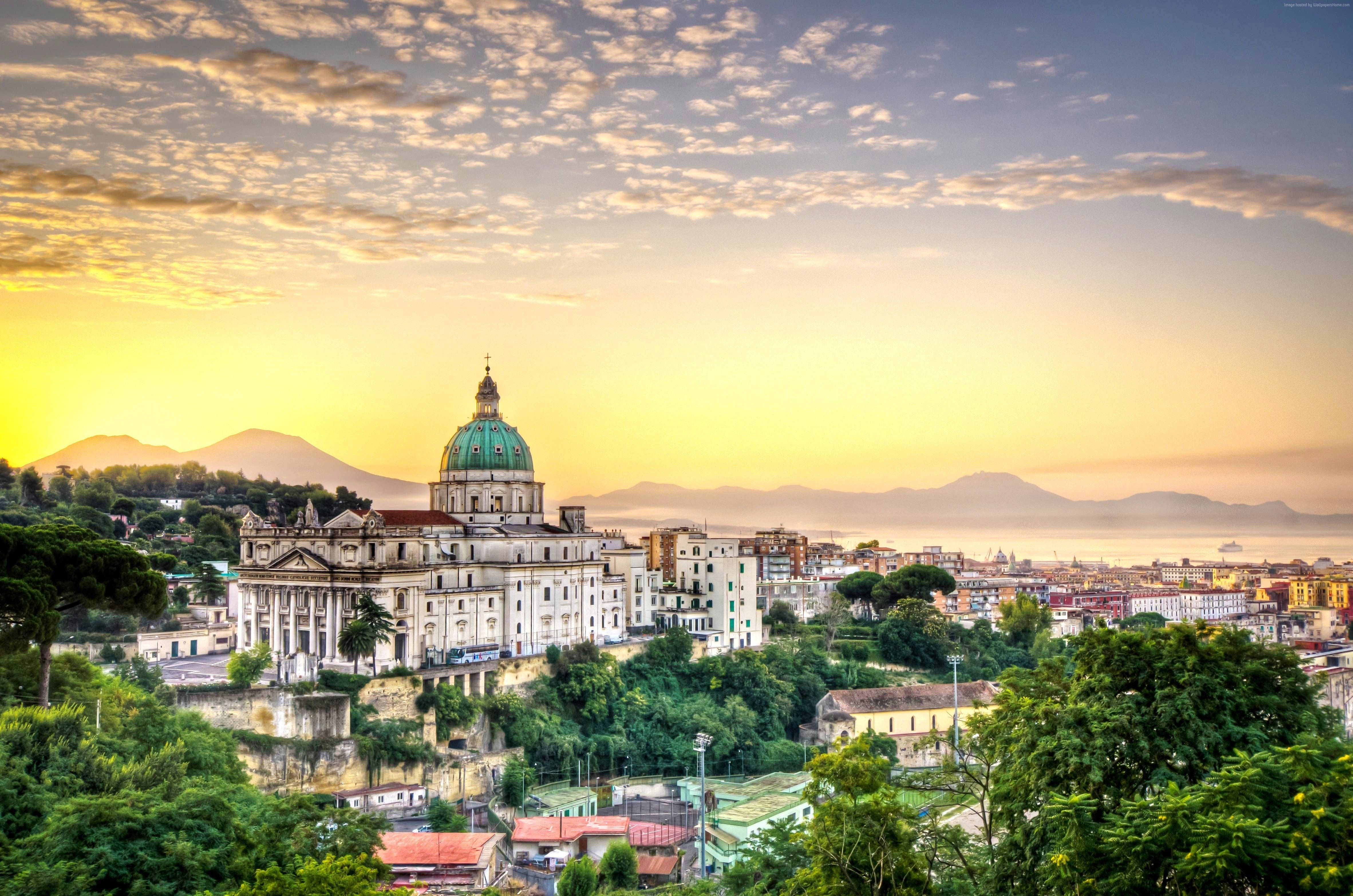 Naples 桌布 壁紙 — 一座擁有綠色圓頂的大教堂在金色日出時分，聳立於陽光普照的海岸城市之上，該城市坐落在鬱鬱蔥蔥的綠色山丘之間。