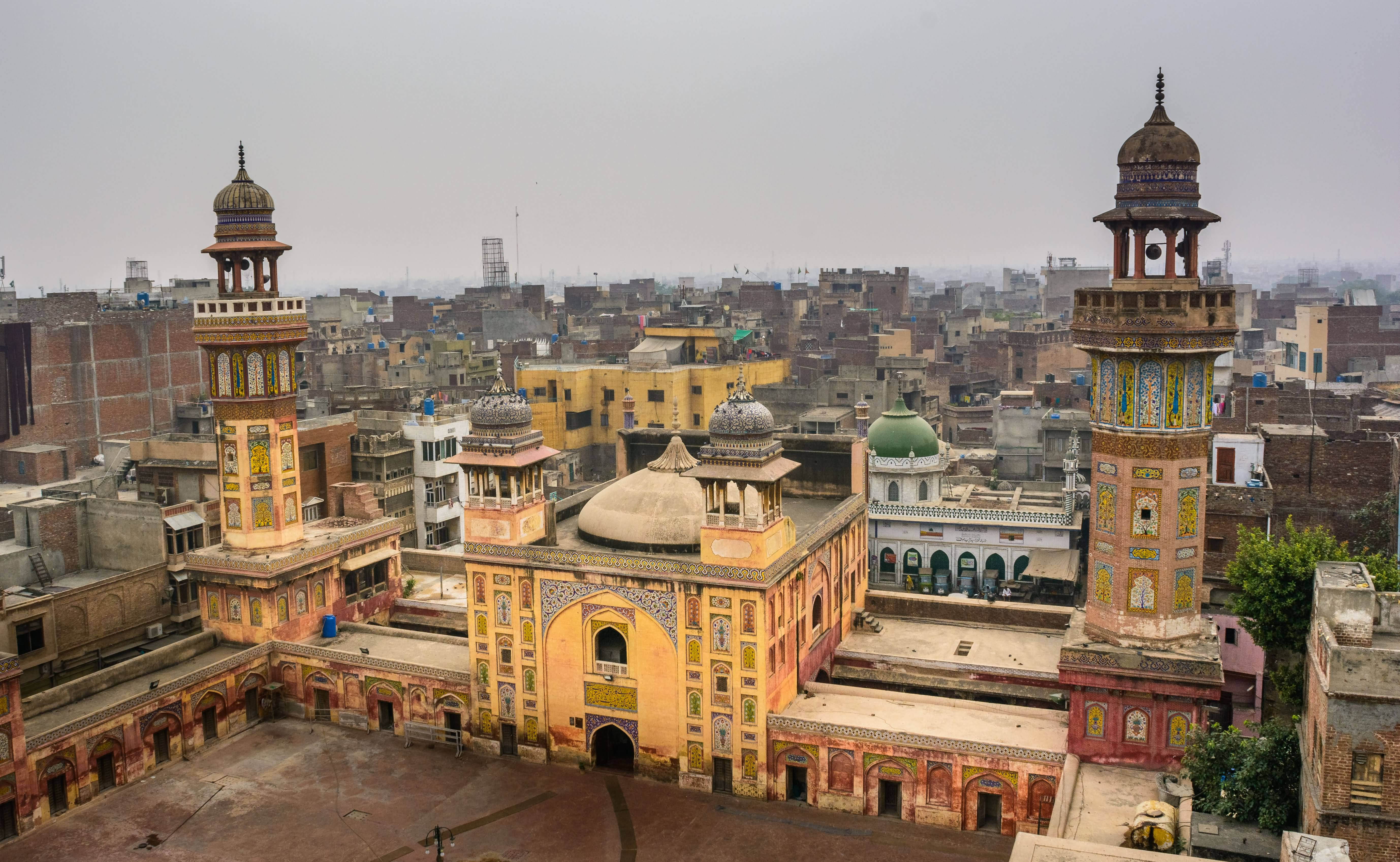 Lahore 桌布 壁紙 — 一座擁有華麗宣禮塔和圓頂的歷史清真寺，在霧濛濛的天空下，於密集的城市擴張中脫穎而出。