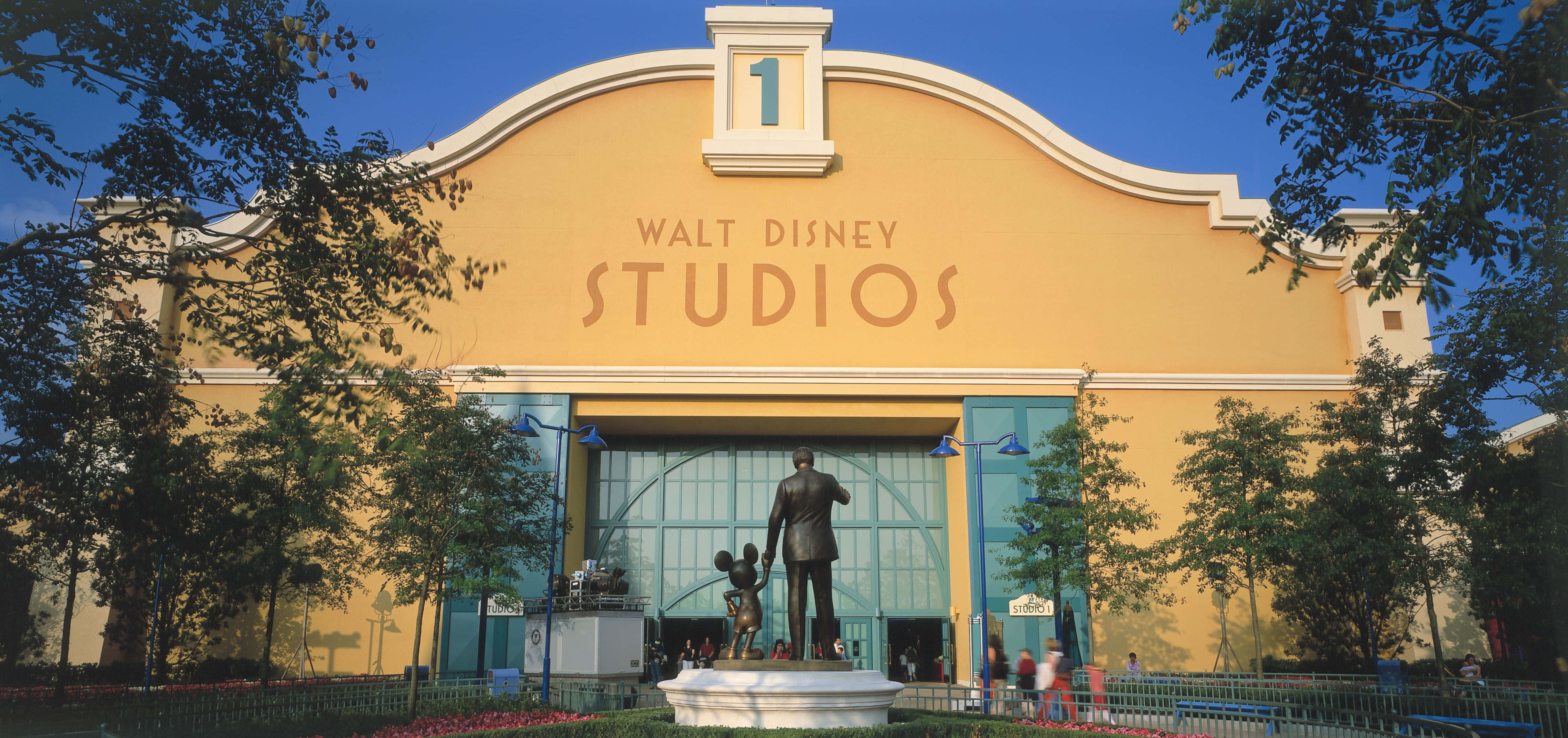 Walt Disney Studios Motion 桌布 壁紙 — 一座明亮的黃色華特迪士尼工作室建築，在清澈的藍天下有米奇老鼠和華特迪士尼的雕像。