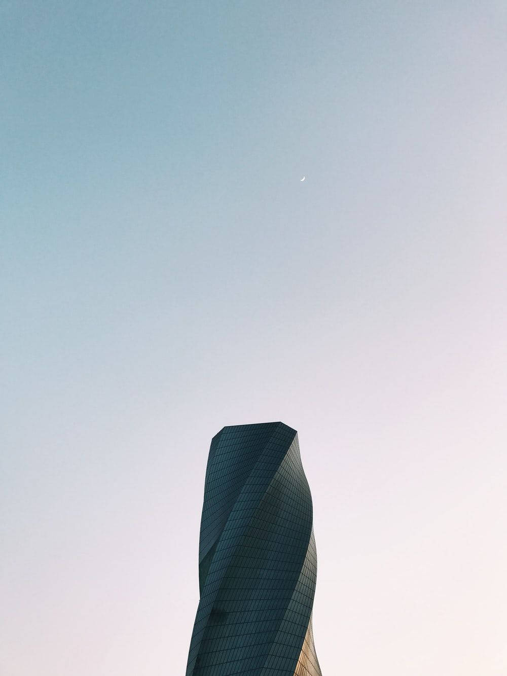 巴林 桌布 壁紙 — 一座時尚扭曲的摩天大樓在柔和漸變的天空中升起，上方可見一彎新月。