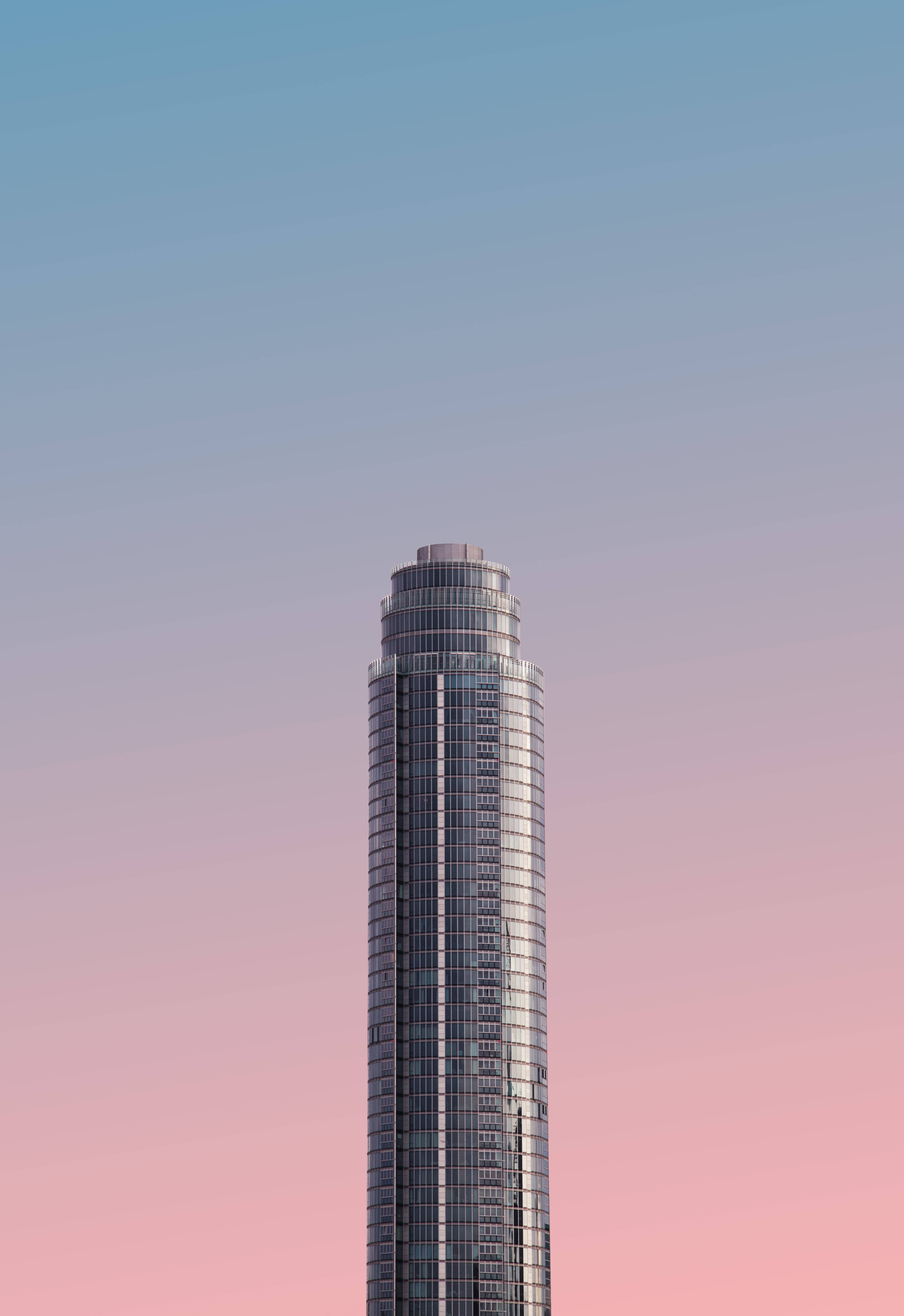 Shapes 桌布 壁紙 — 一座時尚的玻璃摩天大樓刺穿柔和的漸變天空，在黃昏時分從藍色過渡到粉紅色。