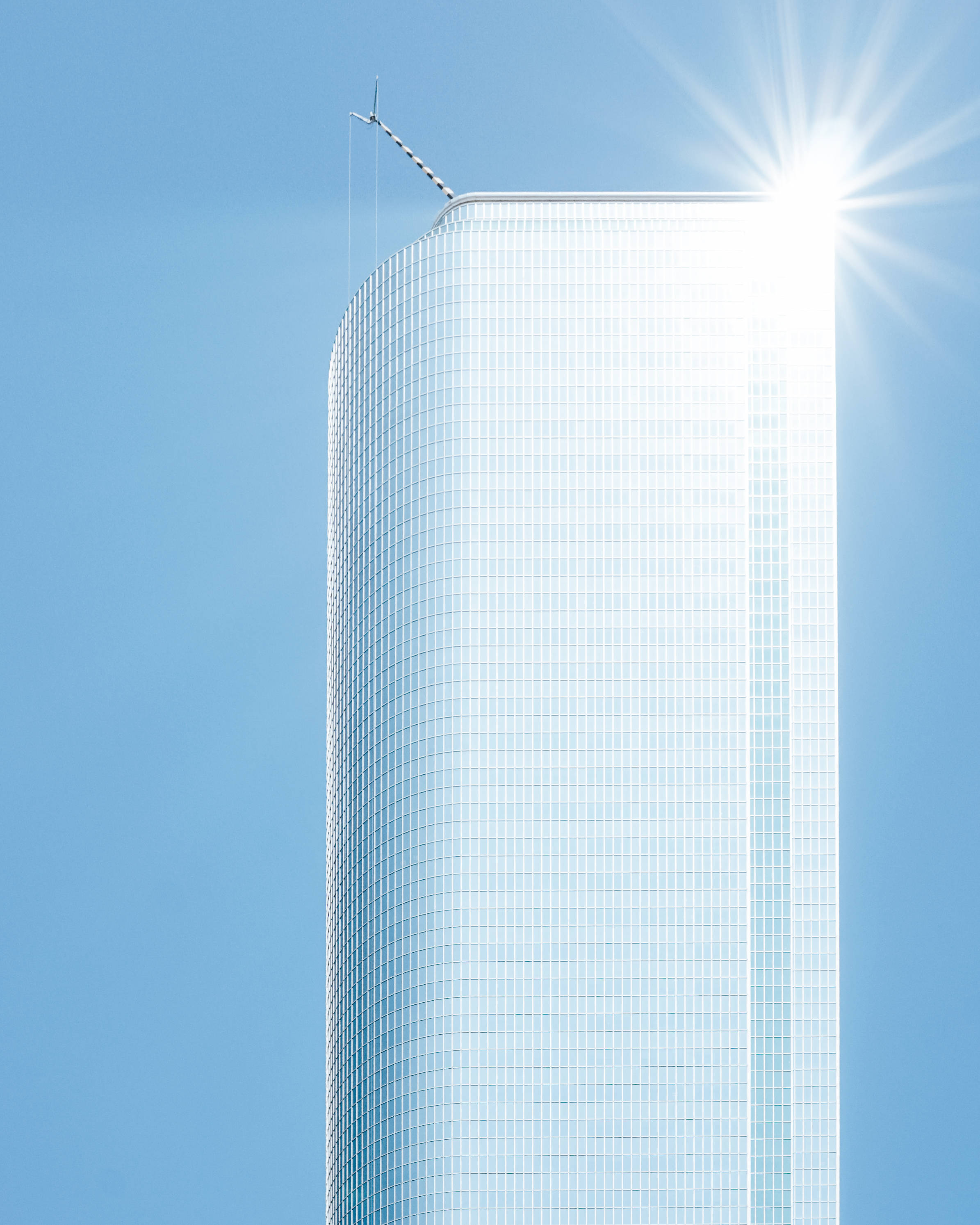 Skyscraper 桌布 壁紙 — 一座時尚的玻璃摩天大樓在清澈的藍天下向上彎曲，太陽在其頂端燦爛地照耀。