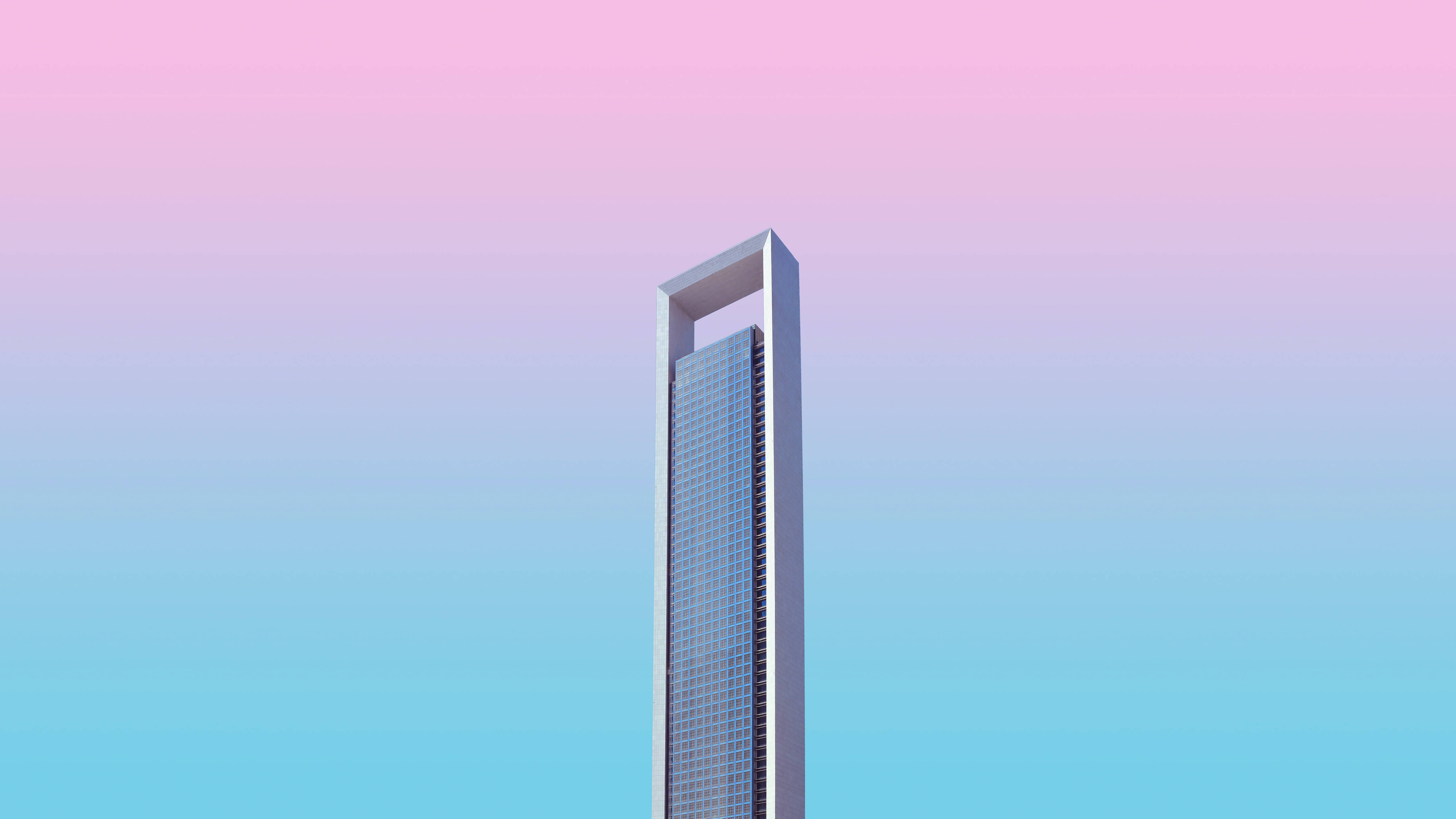 Pretty Pastel 桌布 壁紙 — 一座時尚的現代摩天大樓，頂部有獨特的環形，在柔和的粉紅到藍色漸變天空下高聳入雲。