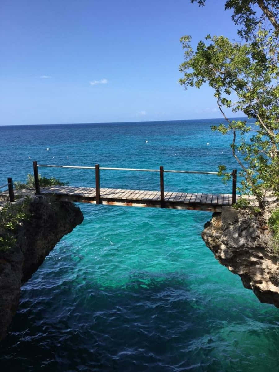 Jamaica 桌布 壁紙 — 一座木橋橫跨岩石懸崖之間的碧綠海洋裂縫，上方是清澈的藍天。