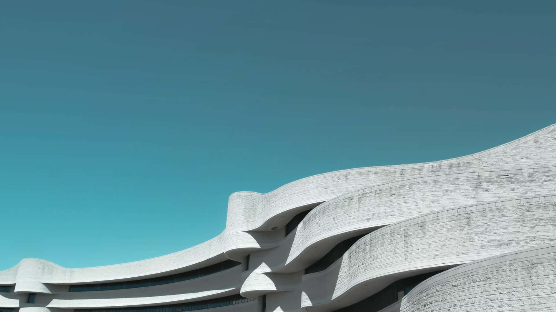 建築 桌布 壁紙 — 一座未來主義風格的白色建築結構，帶有流暢的曲線，矗立在清澈的藍綠色天空下。