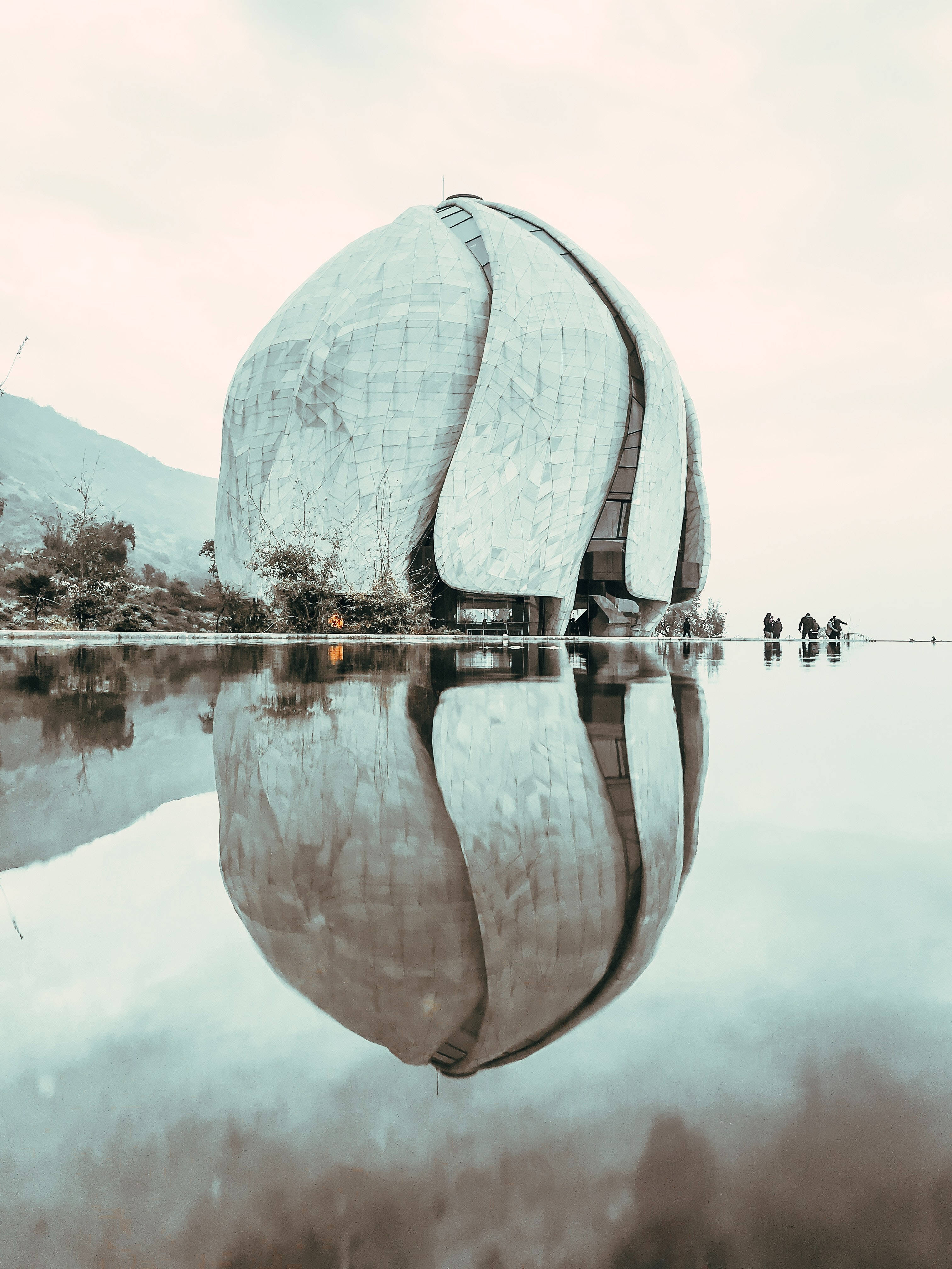 建築 桌布 壁紙 — 一座未來風格的圓頂建築，帶有紋理金屬表面，完美倒映在陰天下一片平靜淺水之中。