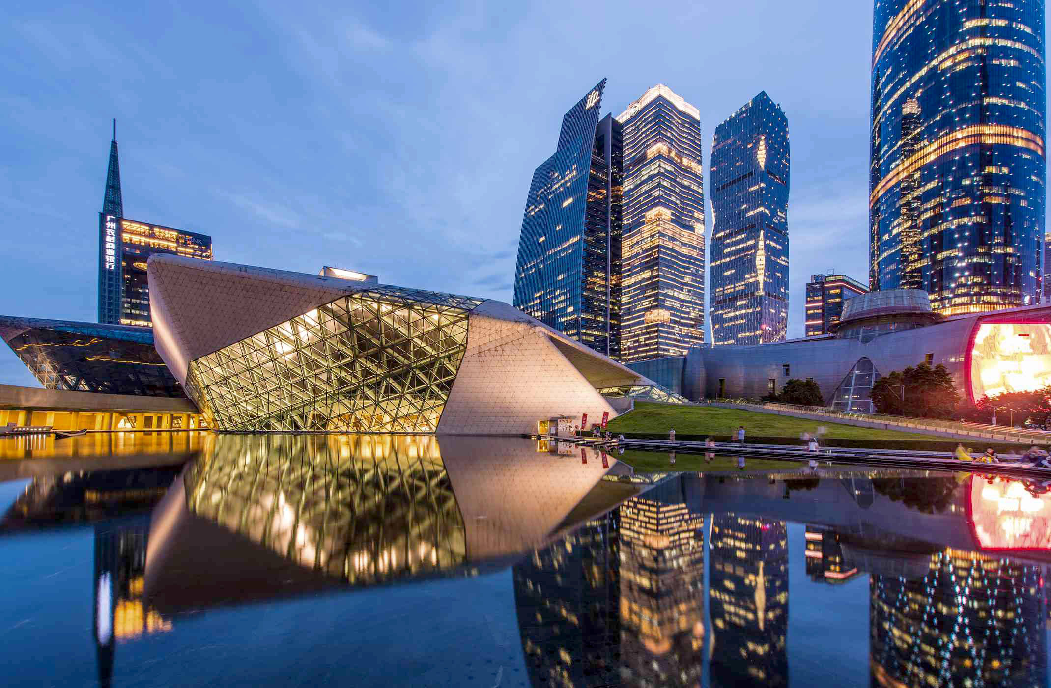 Guangzhou 桌布 壁紙 — 一座未來風格的玻璃和鋼鐵建築在平靜的水面上倒映，旁邊是高聳的摩天大樓，在暮色天空下。