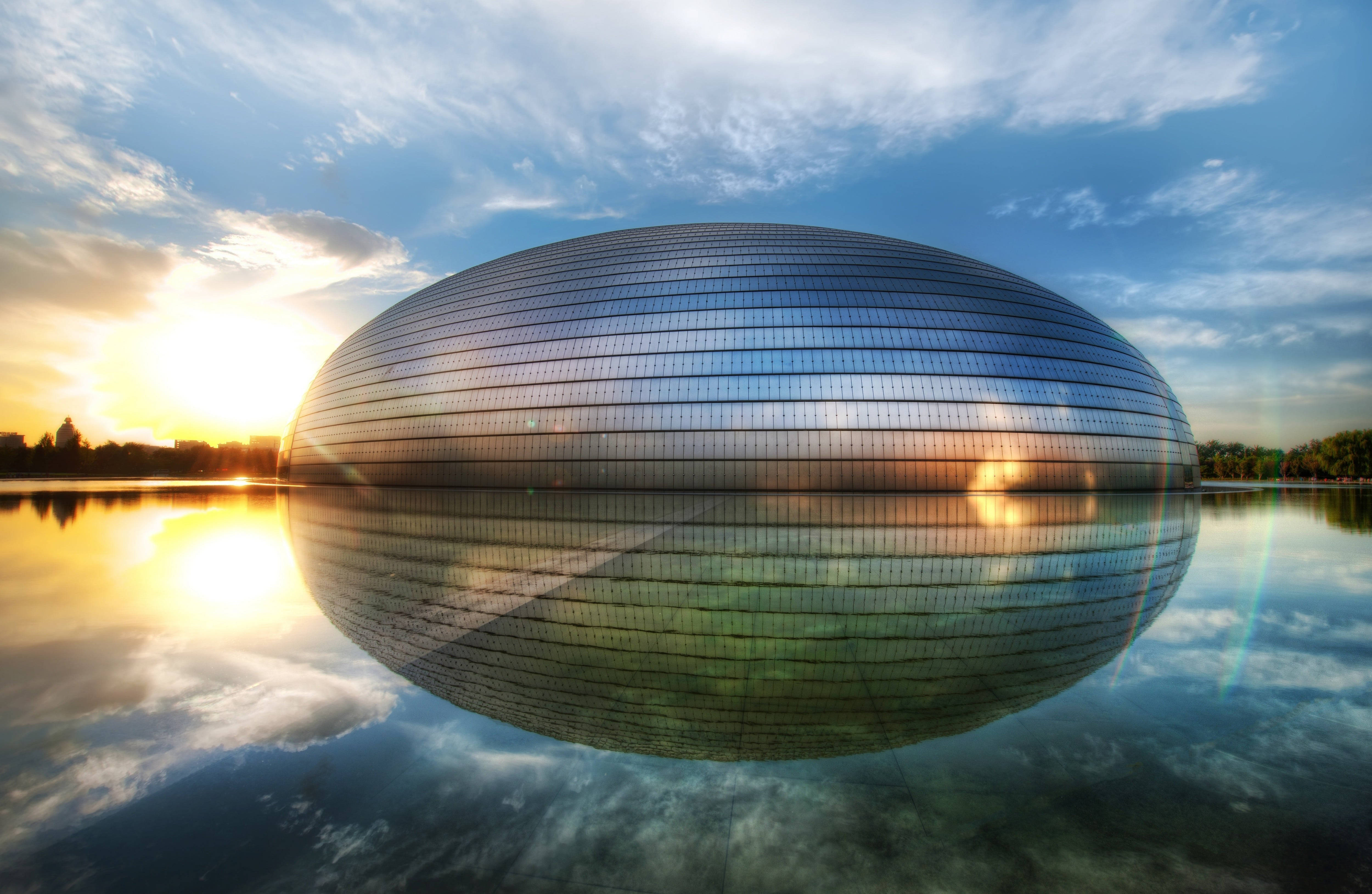 Beijing 桌布 壁紙 — 一座未來風格的玻璃圓頂建築完美倒映在平靜的水面上，金色的夕陽光芒沐浴著天空和建築。