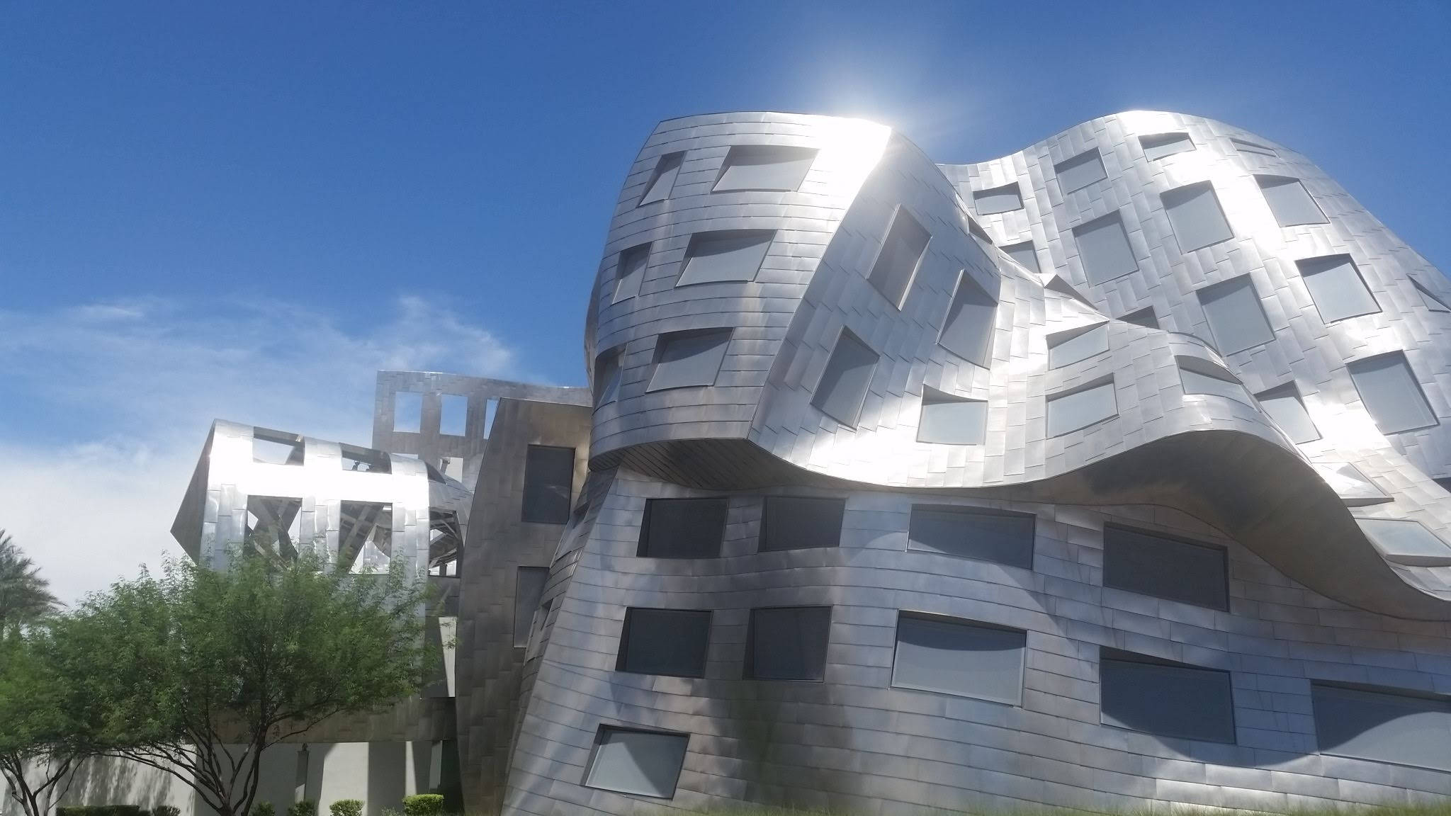 高清 桌布 壁紙 — 一座未來風格的銀色建築，帶有波浪形金屬面板和幾何窗戶，在清澈的藍天下閃閃發光。