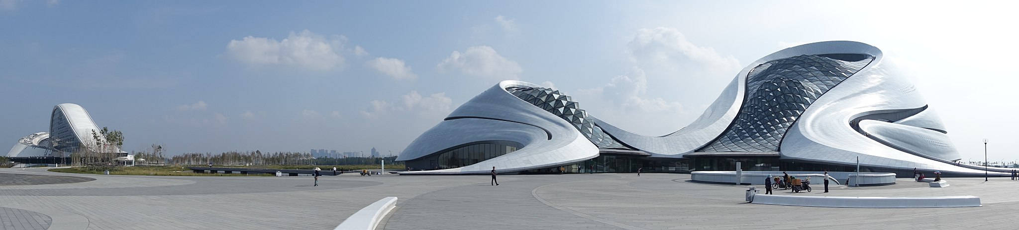 Harbin 桌布 壁紙 — 一座未來風格的銀色建築，擁有流暢曲線和玻璃面板，在明亮的藍天和散落的雲朵下。