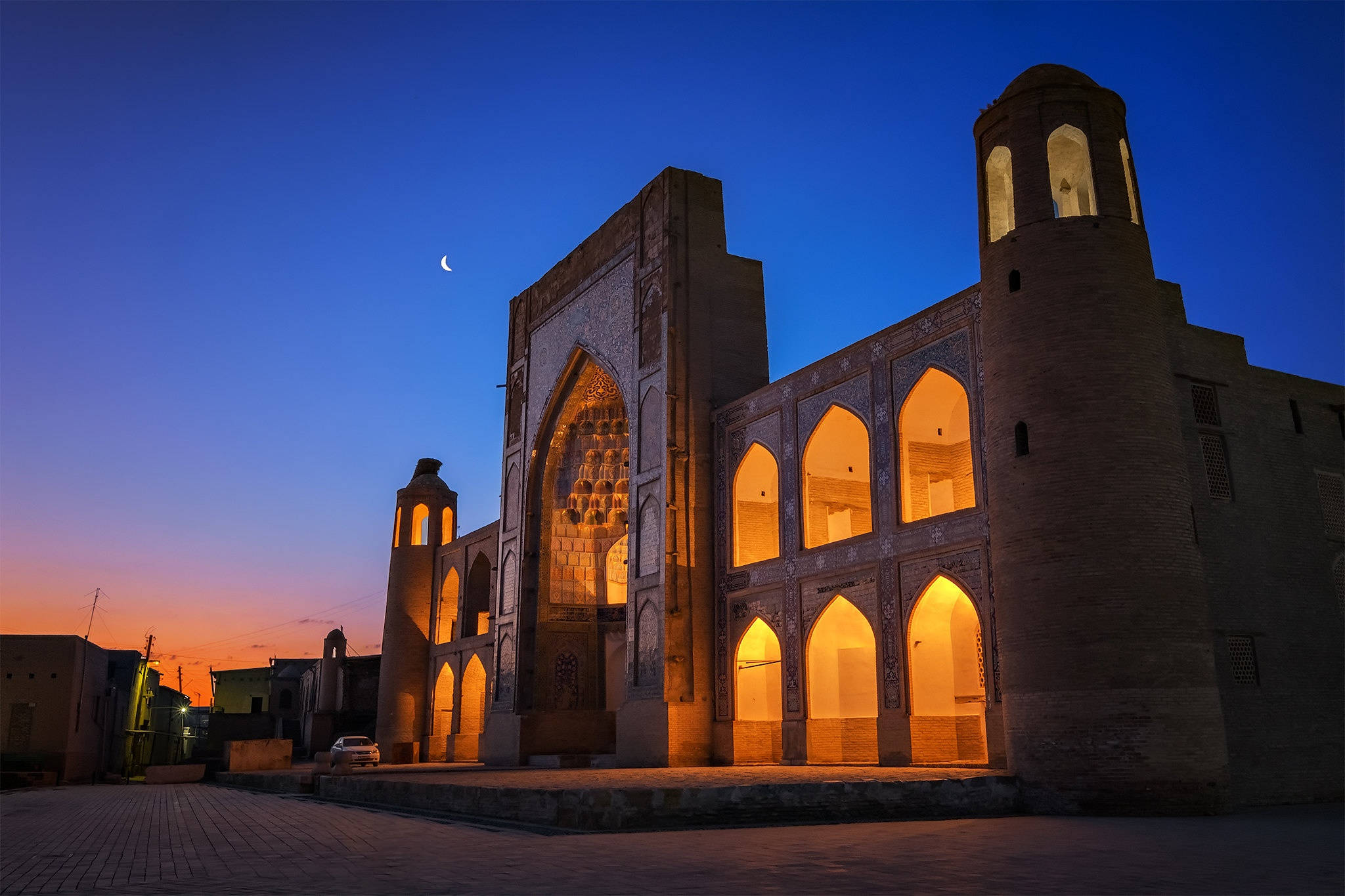 Uzbekistan 桌布 壁紙 — 一座歷史悠久的伊斯蘭建築群在黃昏時分溫暖地發光，新月懸掛在其拱形窗戶和宣禮塔之上。
