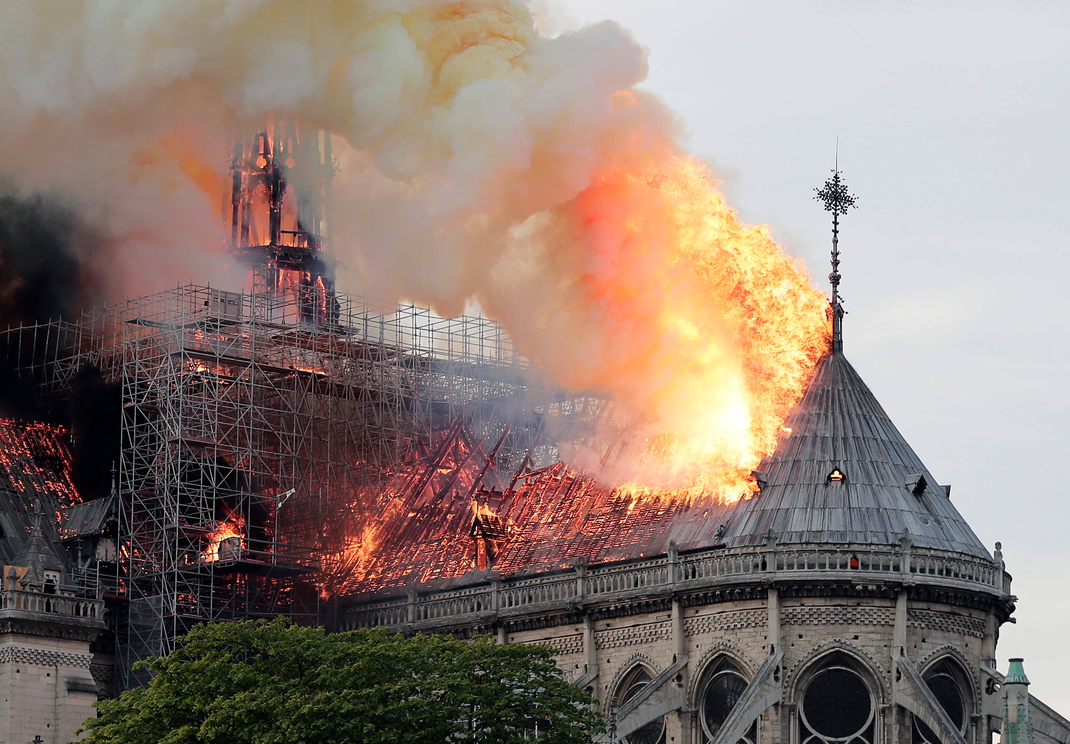 Notre Dame 桌布 壁紙 — 一座歷史悠久的大教堂在灰濛濛的天空下猛烈燃燒，橙色的火焰和濃煙從屋頂滾滾冒出。
