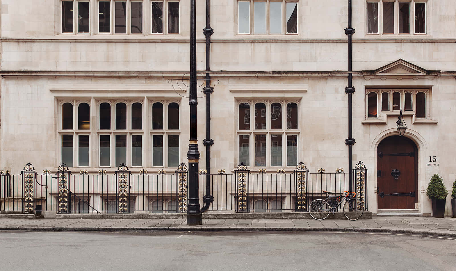 Architecture 桌布 壁紙 — 一座歷史悠久的奶油色石建築，擁有拱形窗戶和木門，矗立在華麗的黑色鐵柵欄後面，旁邊停著一輛自行車。