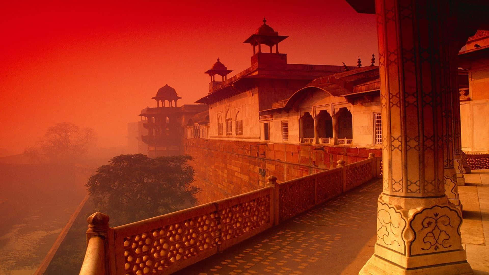 Indian 桌布 壁紙 — 一座歷史悠久的宮殿，在朦朧的日出中沐浴在火紅橙色的光芒中，擁有精緻的石欄杆和圓頂塔樓。