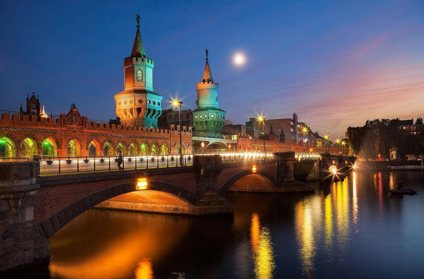 Berlin 桌布 壁紙 — 一座歷史悠久的橋樑，帶有燈光照明的高塔，在暮色中橫跨河流，上方有一輪滿月。