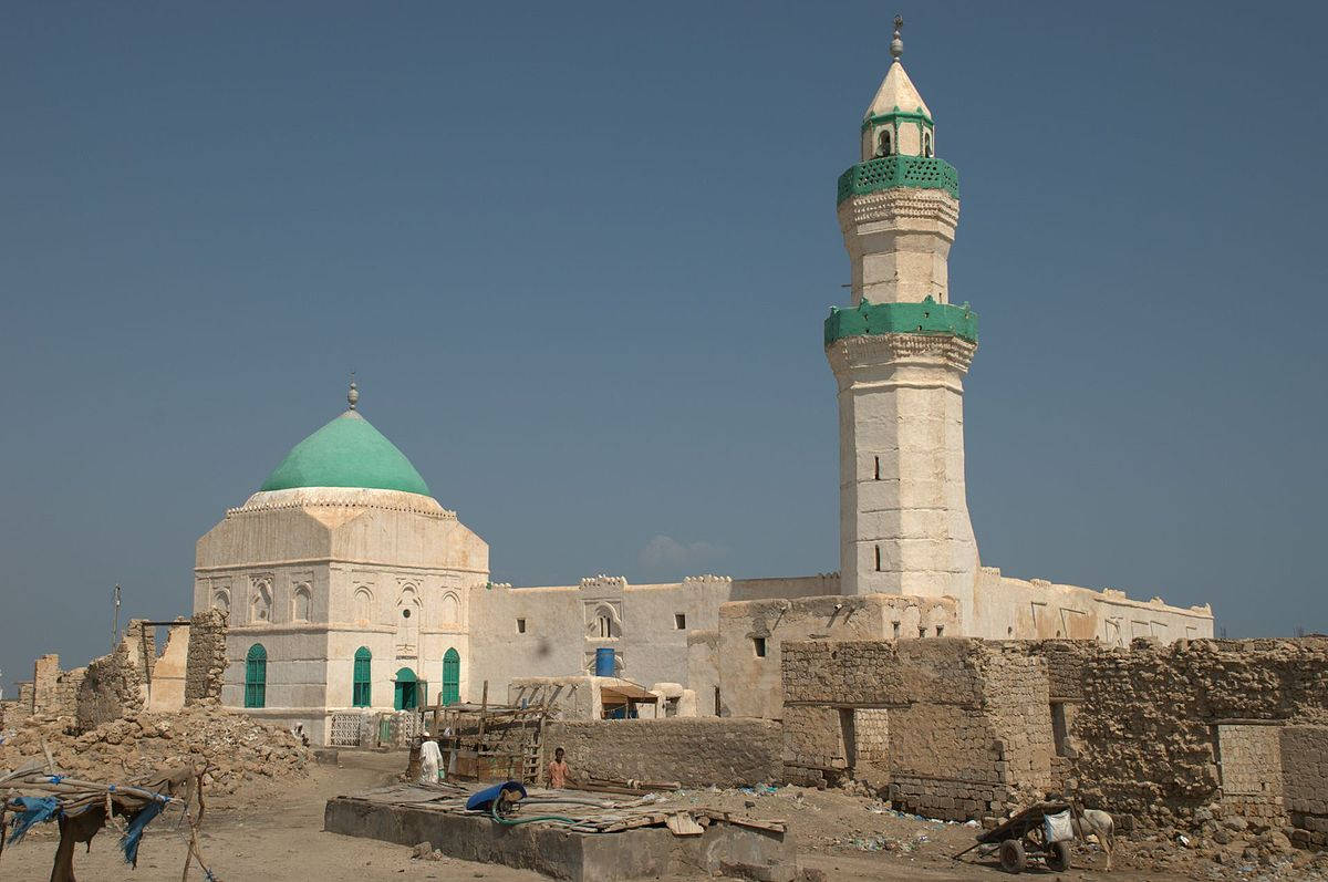 Sudan 桌布 壁紙 — 一座歷史悠久的清真寺，擁有藍綠色圓頂和宣禮塔，在塵土飛揚、部分廢墟的城市環境中，矗立在清澈的藍天下。