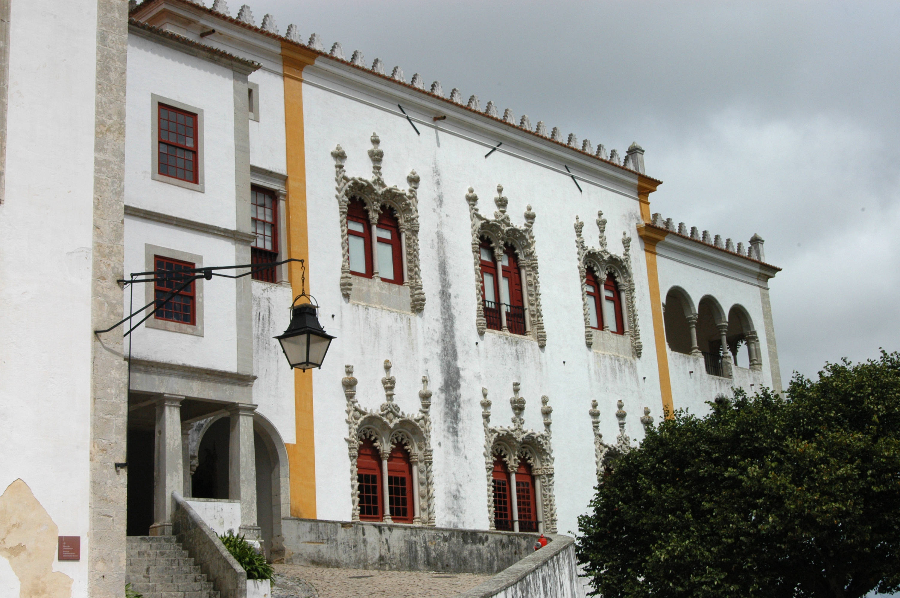 Portugal 桌布 壁紙 — 一座歷史悠久的白色建築，帶有華麗的石雕和紅色窗戶，位於多雲的天空下。