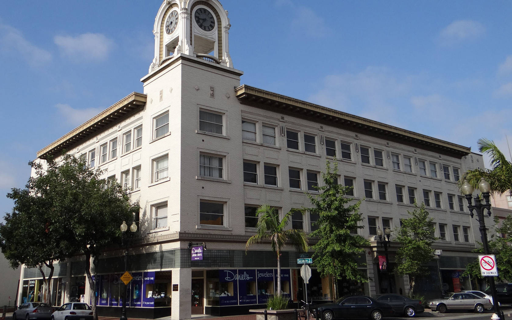 Building 桌布 壁紙 — 一座歷史悠久的白色鐘樓建築聳立在陽光明媚的城市角落，下方有棕櫚樹和停泊的汽車。