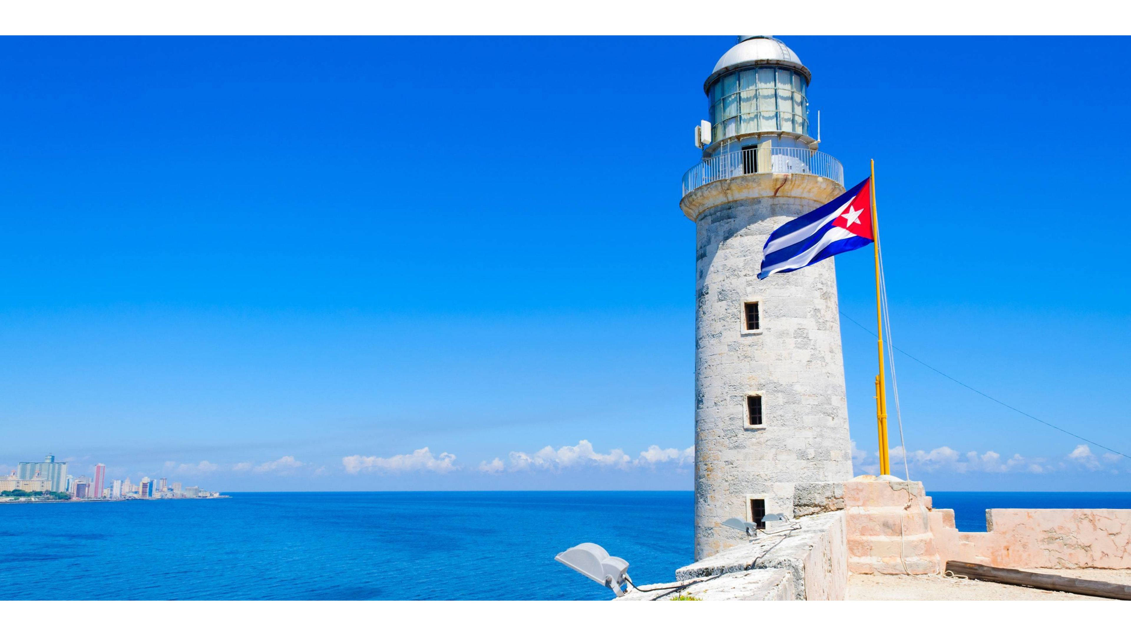 Cuban 桌布 壁紙 — 一座歷史悠久的石造燈塔矗立在海邊懸崖上，古巴國旗在清澈的藍天和碧綠的海洋中驕傲地飄揚。