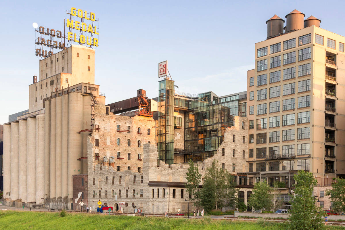 Minneapolis 桌布 壁紙 — 一座歷史悠久的穀物升降機，帶有發光的「Gold Medal Flour」標誌，矗立在一棟現代玻璃建築旁邊，天空清澈湛藍。