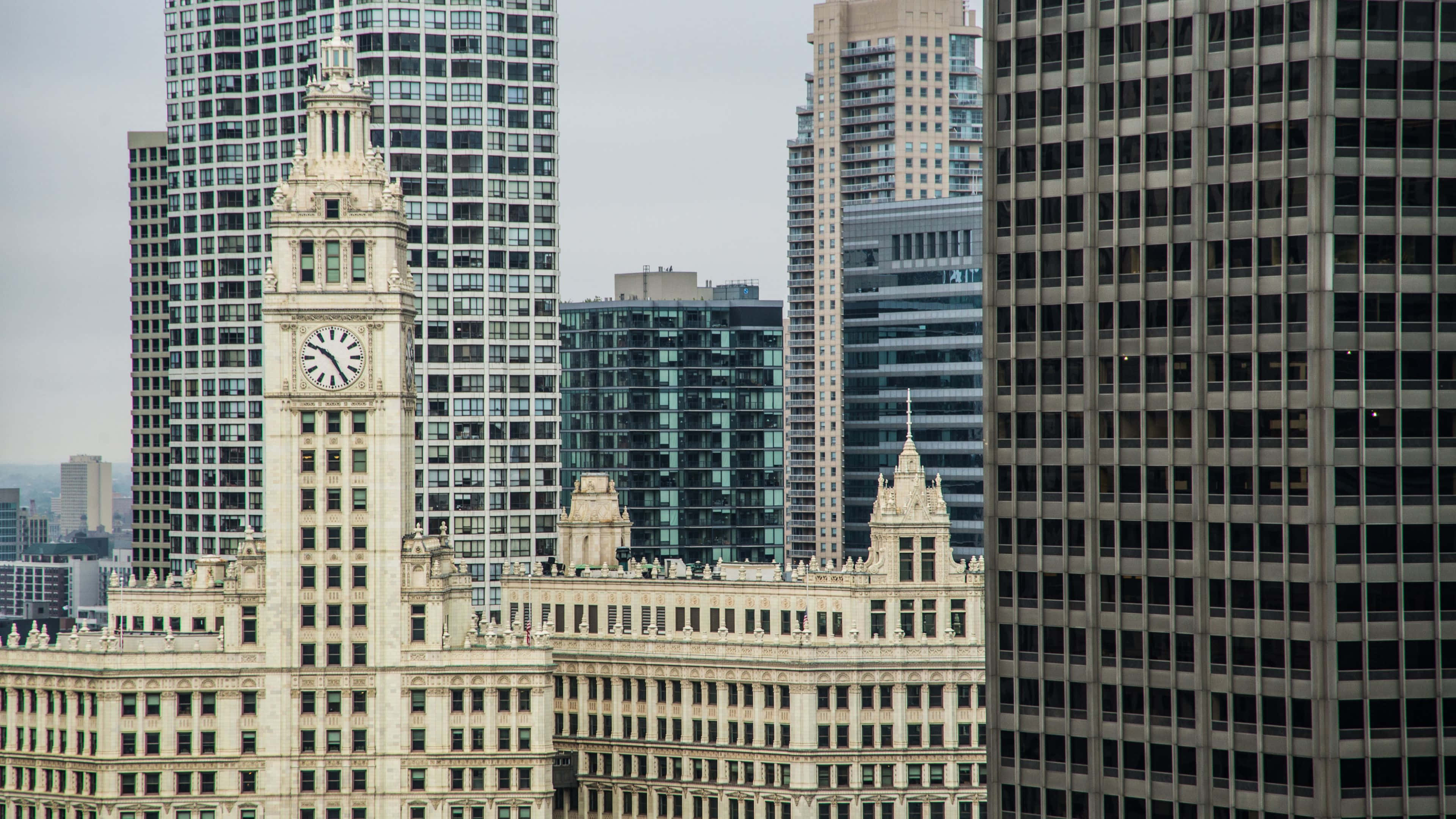 4K Ultra HD Chicago 桌布 壁紙 — 一座歷史悠久的鐘樓建築在陰天之下，突出地矗立於密集的現代摩天大樓群中。