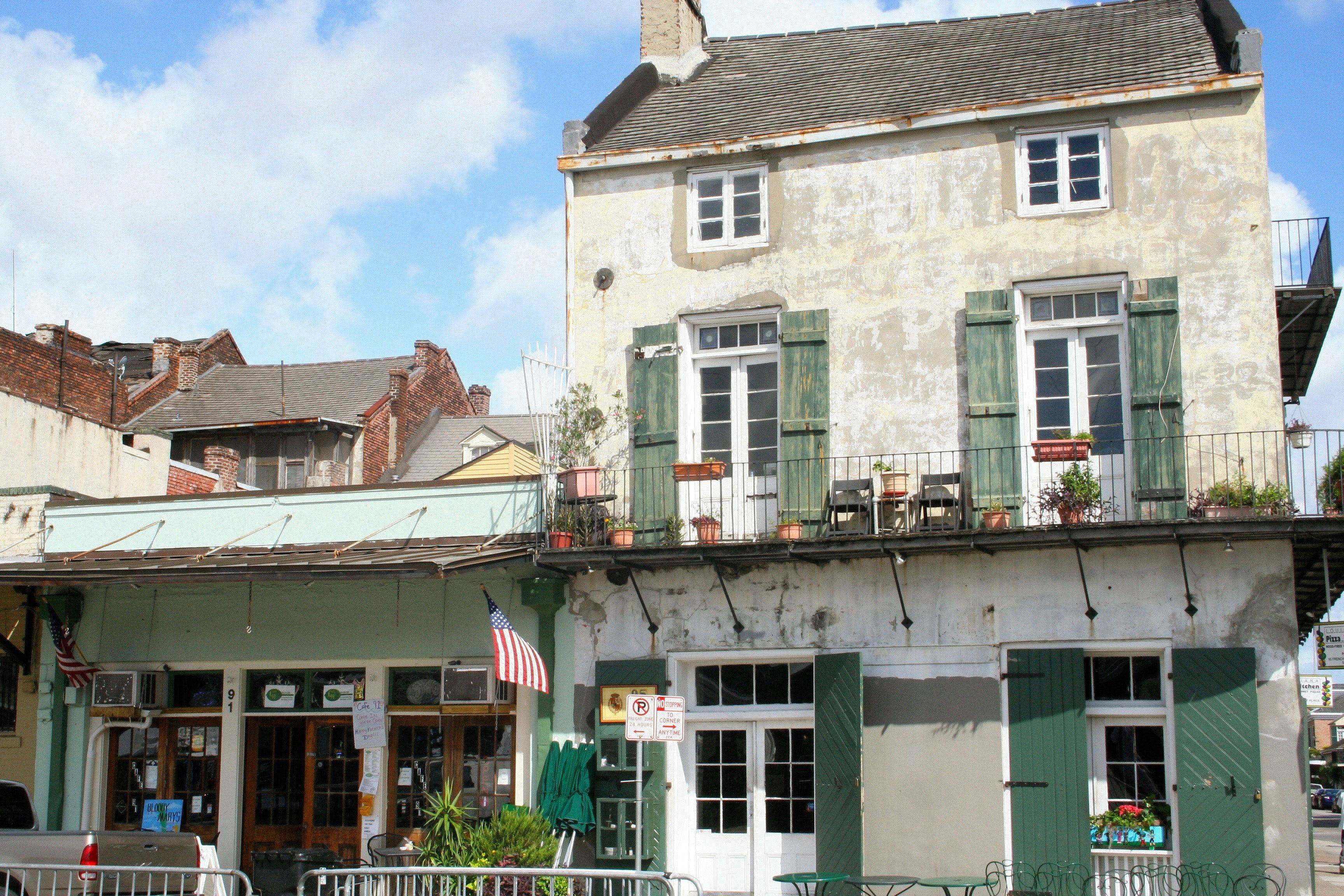french 桌布 壁紙 — 一座歷經風霜的歷史建築，擁有綠色百葉窗和陽台，陽台上擺放著盆栽植物，在明亮的藍天下。