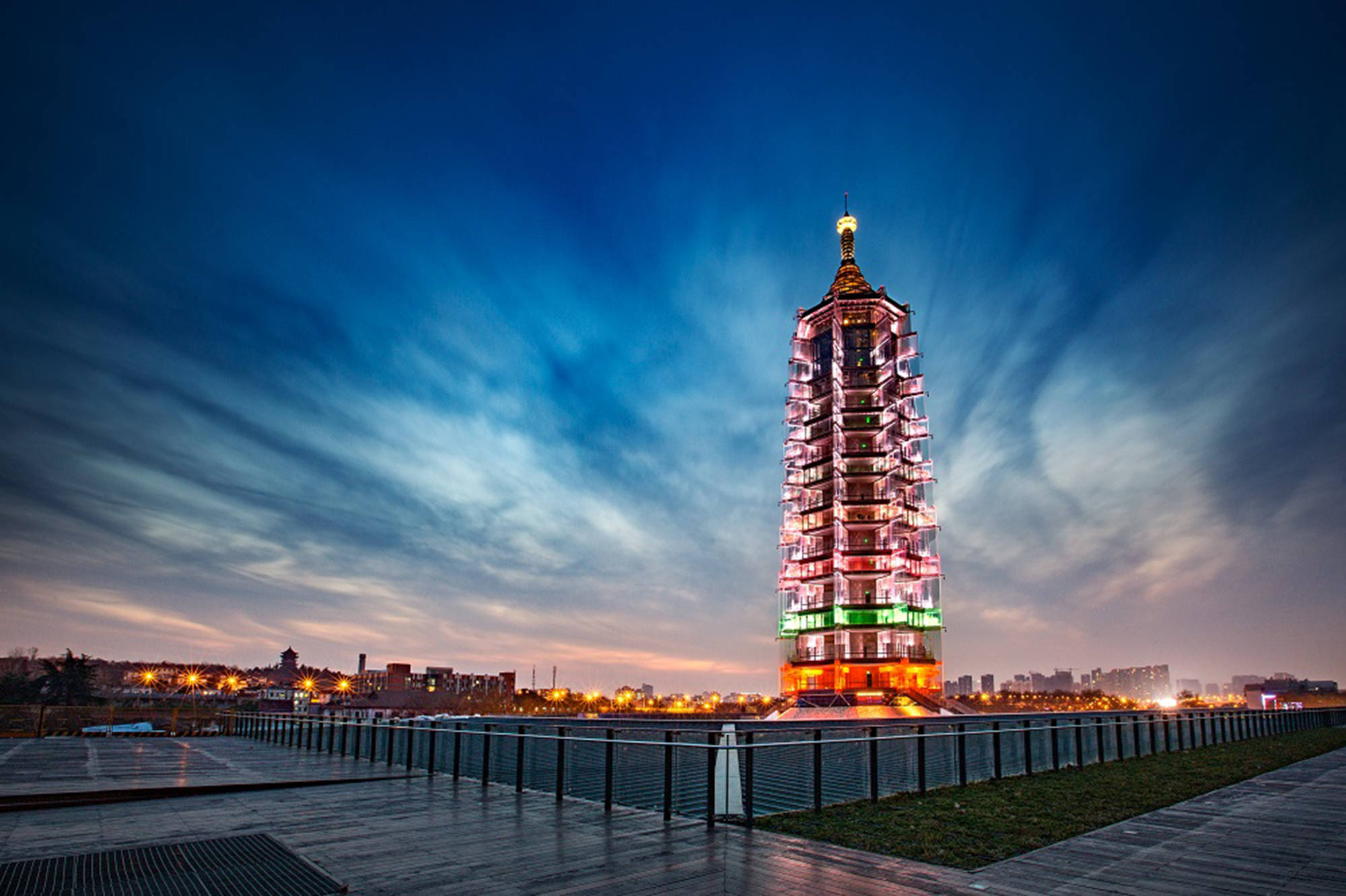 Nanjing 桌布 壁紙 — 一座燈火通明的寶塔高聳入雲，映襯著佈滿縷縷雲彩的戲劇性暮色天空，遠處的城市燈光閃爍。