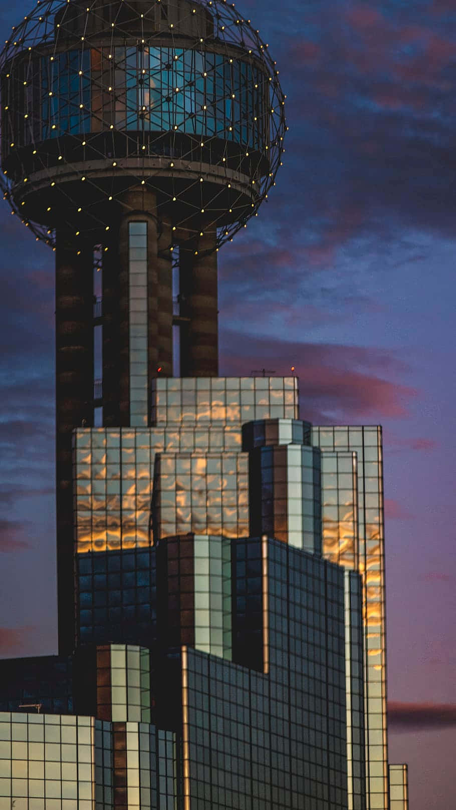 Skyscraper 桌布 壁紙 — 一座玻璃摩天大樓，頂部有一個發光的球形，在暮色天空中反射出溫暖的日落色調。