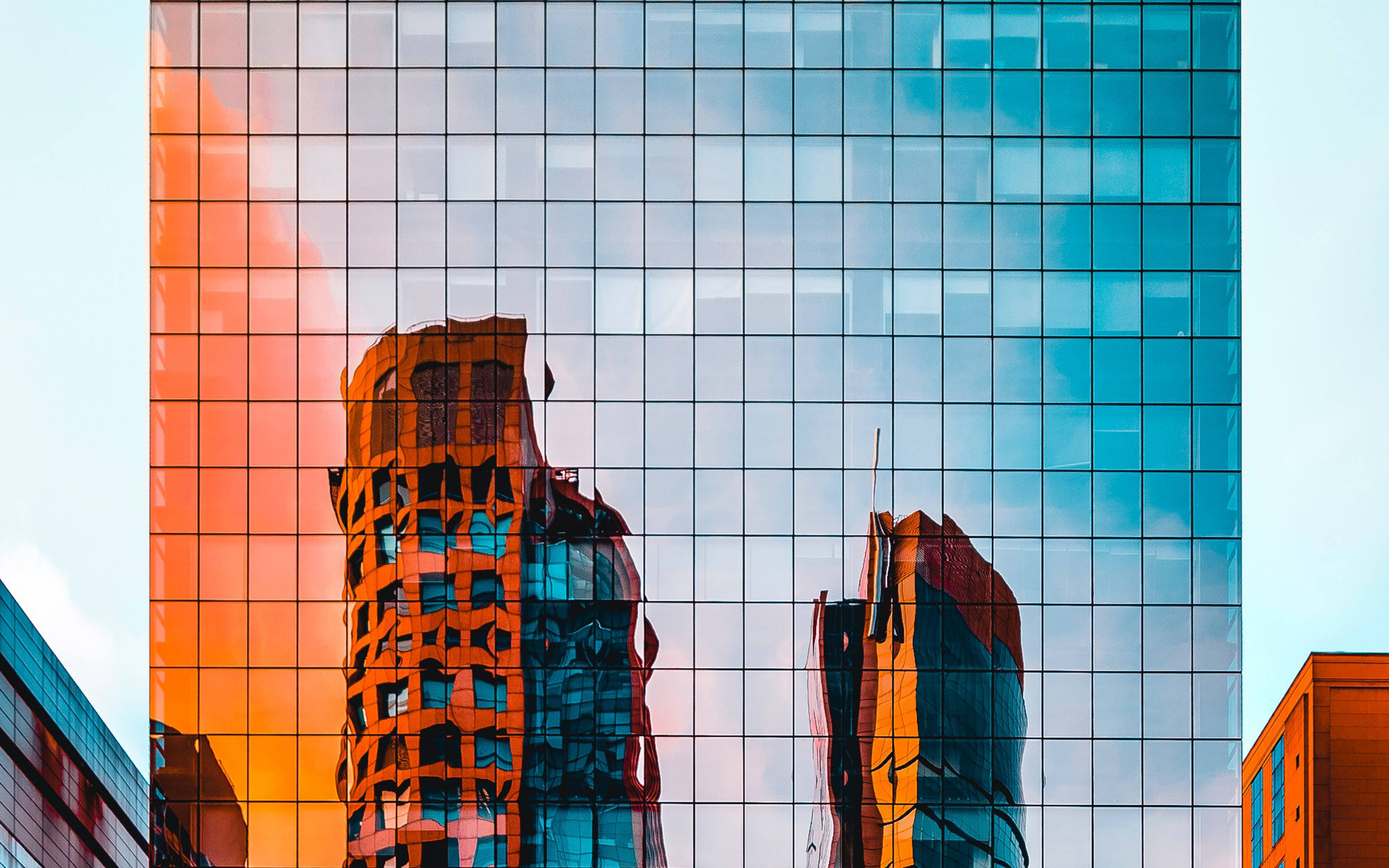 Architecture 桌布 壁紙 — 一座玻璃摩天大樓在蒼白的天空映襯下，反射出火橙色和冷藍色的摩天大樓。