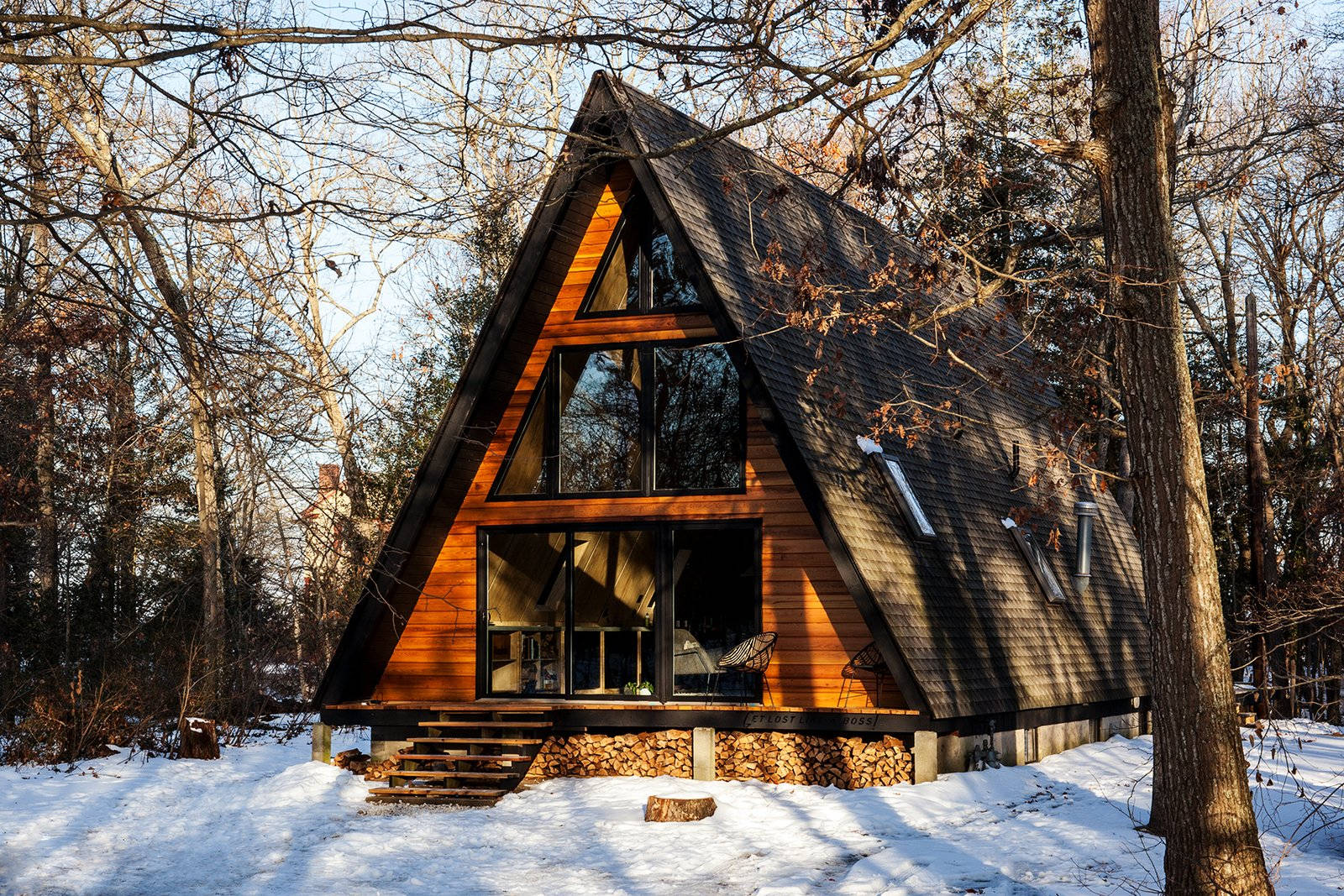 Winter House 桌布 壁紙 — 一座現代A字形小屋，擁有溫暖的木牆和大型玻璃窗，坐落在冬日日出時分的雪林之中。