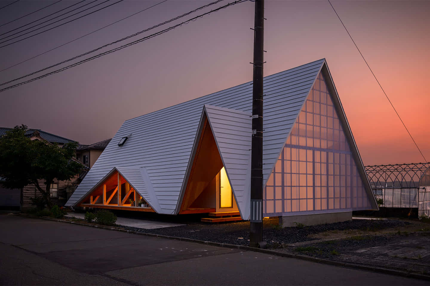 Minimalist Architecture 桌布 壁紙 — 一座現代三角形房屋，內部燈光閃爍，映襯著帶有橙色和紫色色調的暮色天空。