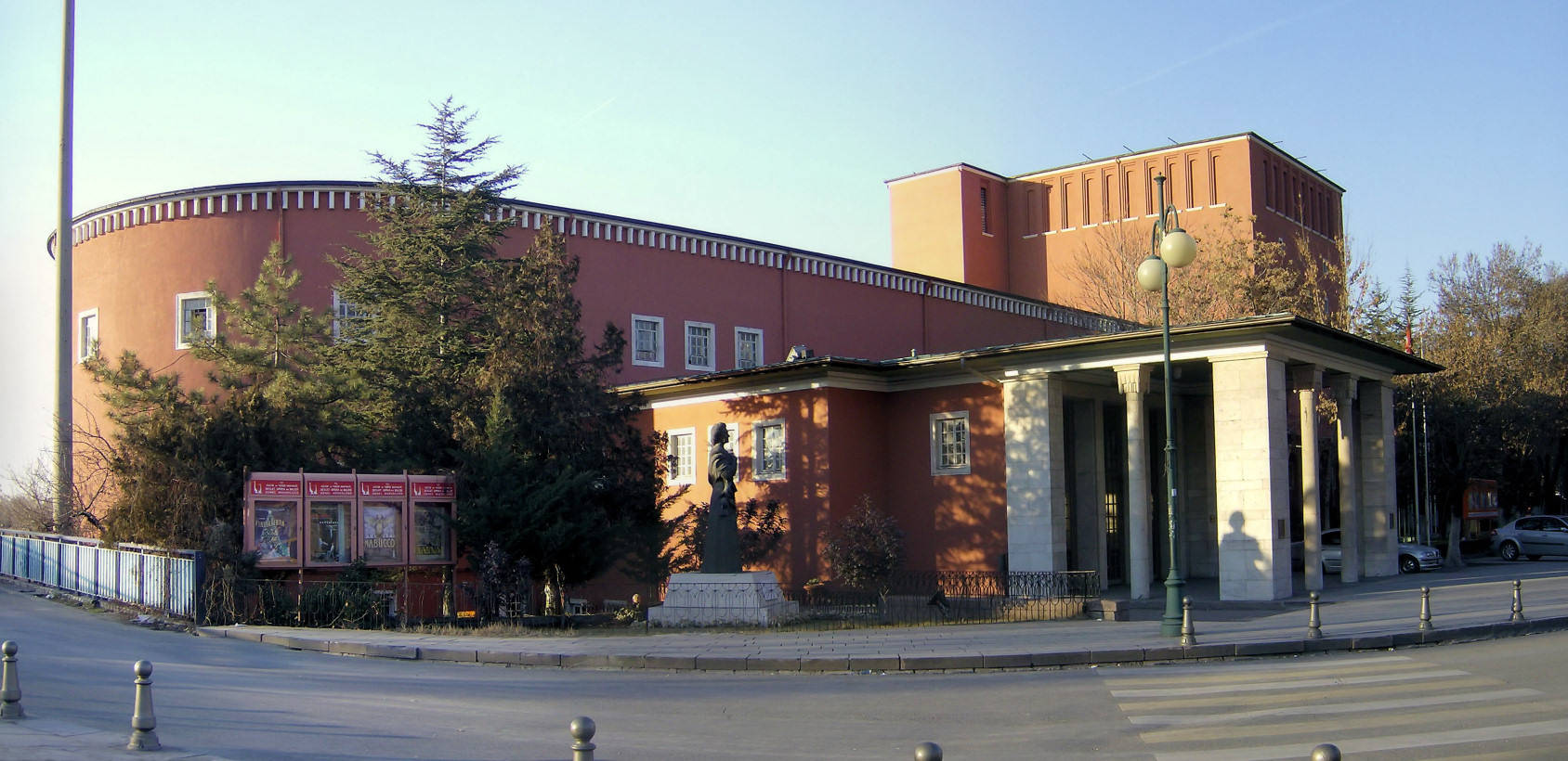 Ankara 桌布 壁紙 — 一座現代主義紅磚建築，擁有弧形外牆和古典柱廊，矗立在街角，上方是晴朗的藍天。