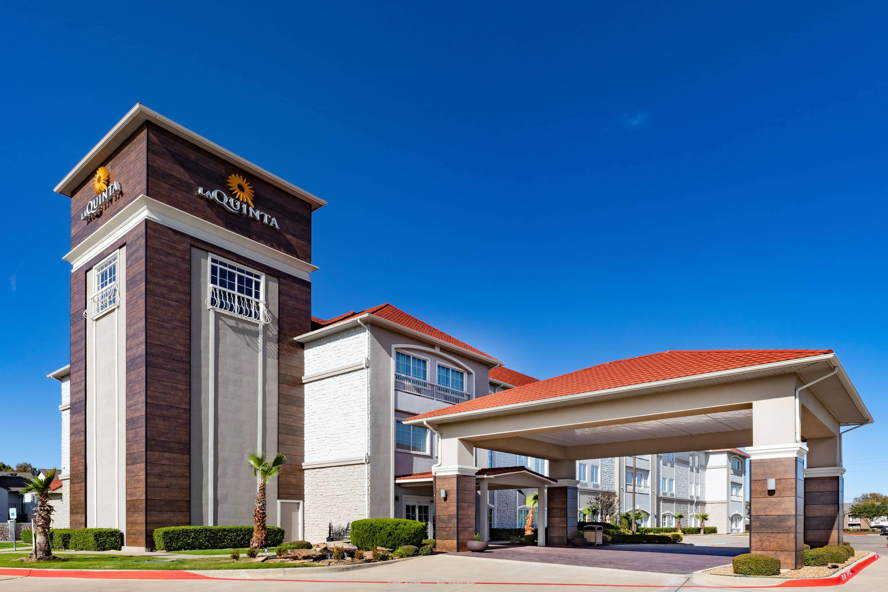 Hotel 桌布 壁紙 — 一座現代化的 La Quinta 飯店建築，在晴朗的藍天下，擁有紅色瓦片屋頂和有蓋入口。