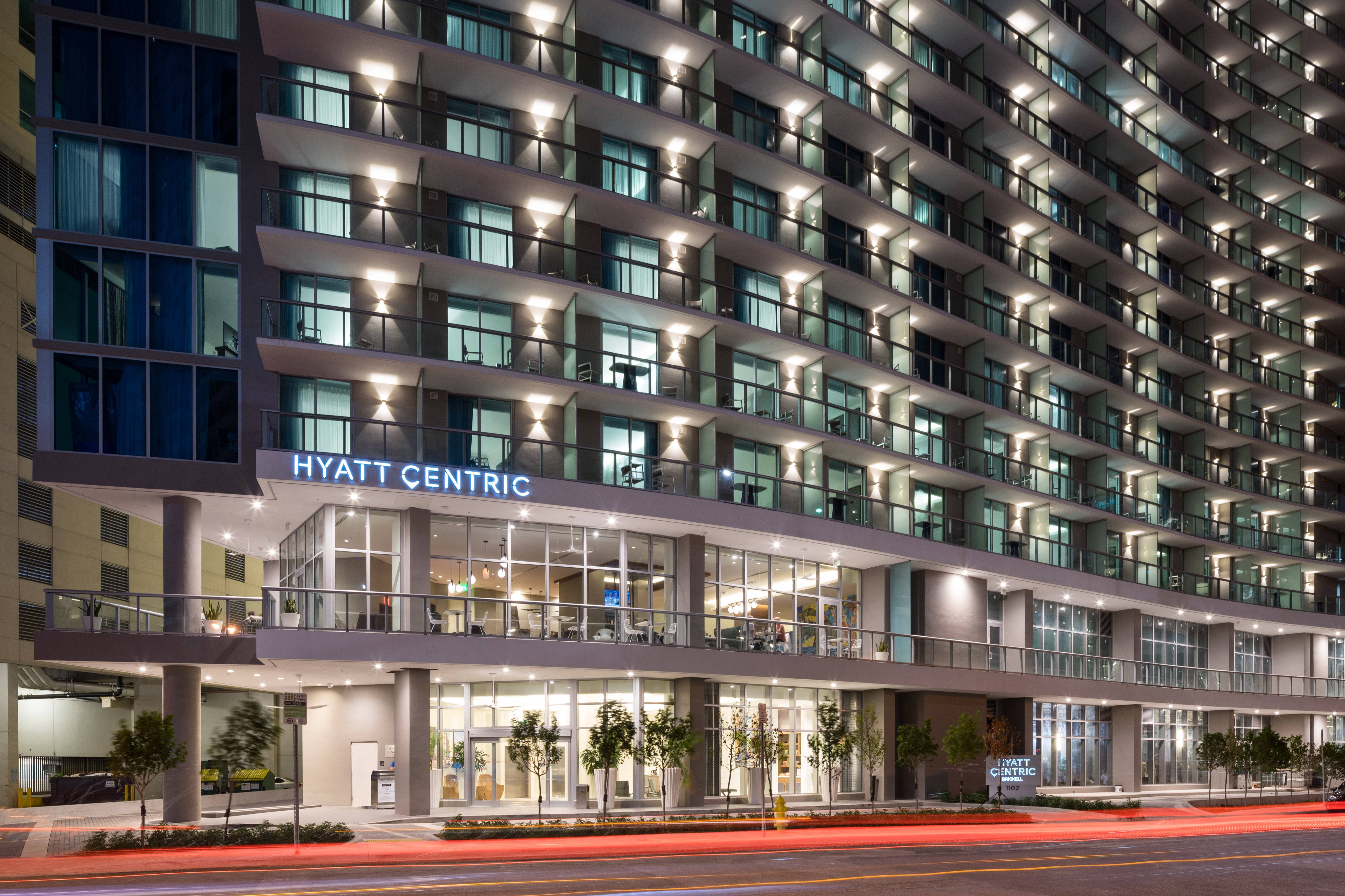 Miami 桌布 壁紙 — 一座現代化的Hyatt Centric酒店建築在夜晚亮起，窗戶發光，下方有紅色交通燈光的痕跡。