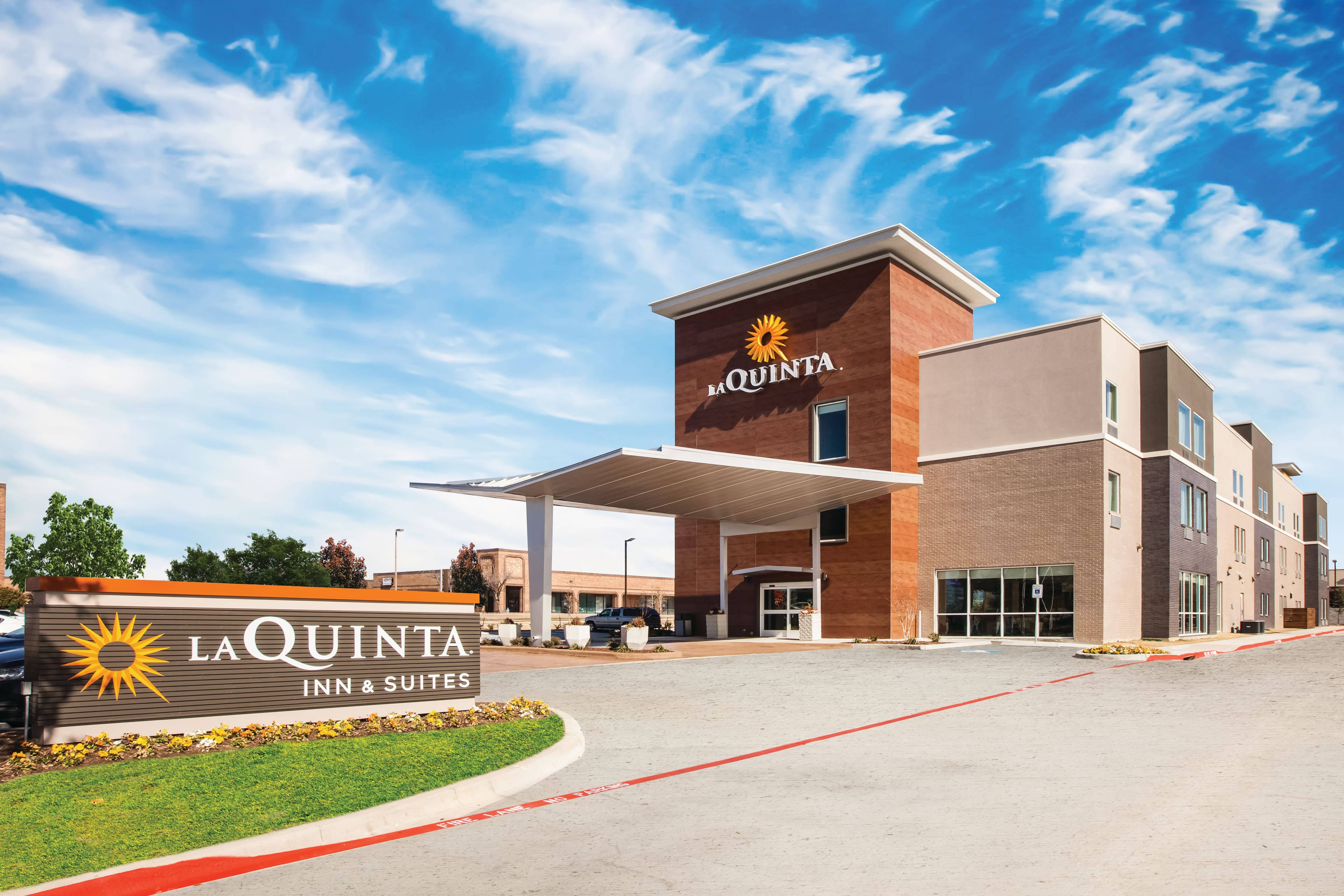 Building 桌布 壁紙 — 一座現代化的La Quinta Inn & Suites酒店建築，在明亮的藍天和薄雲下，前面有一個大型品牌標誌。