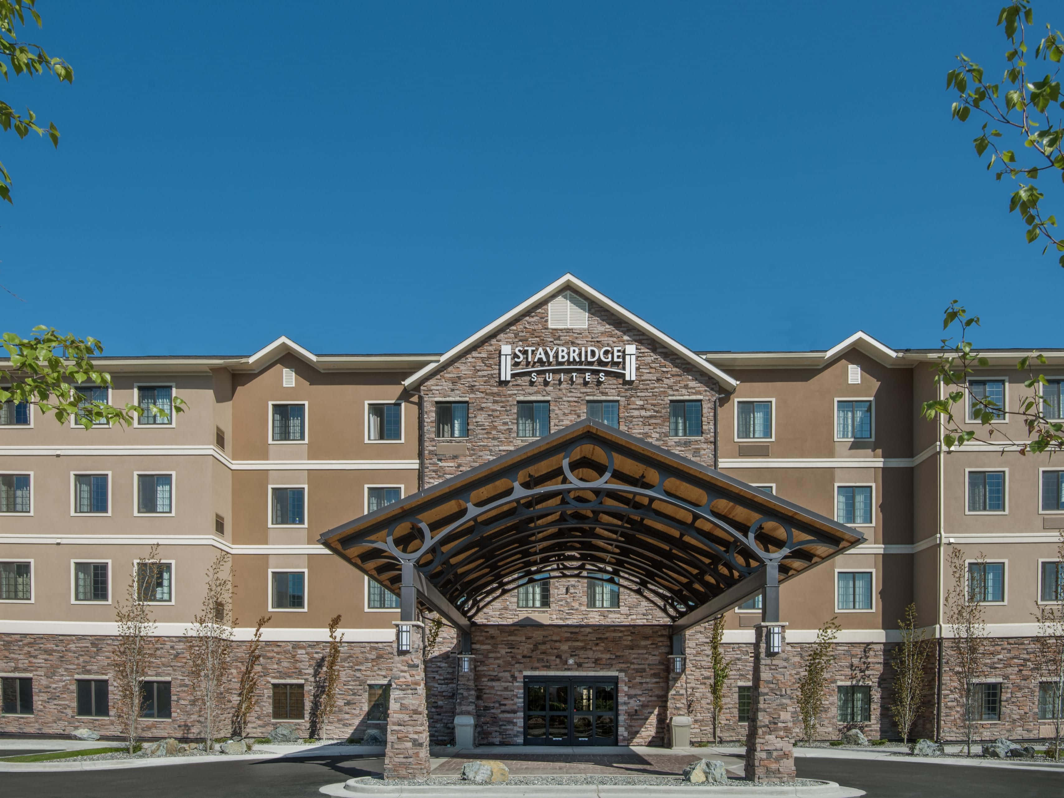 飯店 桌布 壁紙 — 一座現代化的Staybridge Suites酒店建築，在晴朗的藍天下，設有石頭和木材的門廊入口。