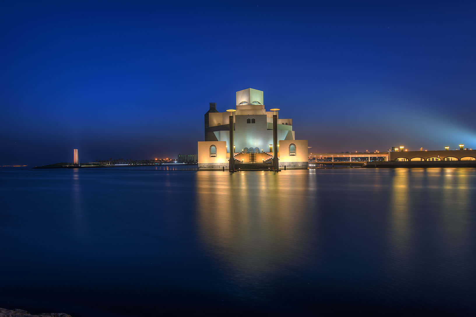 Museum Of Islamic Art 桌布 壁紙 — 一座現代博物館在夜晚亮燈，在深藍色天空下平靜的水面上美麗地倒映。