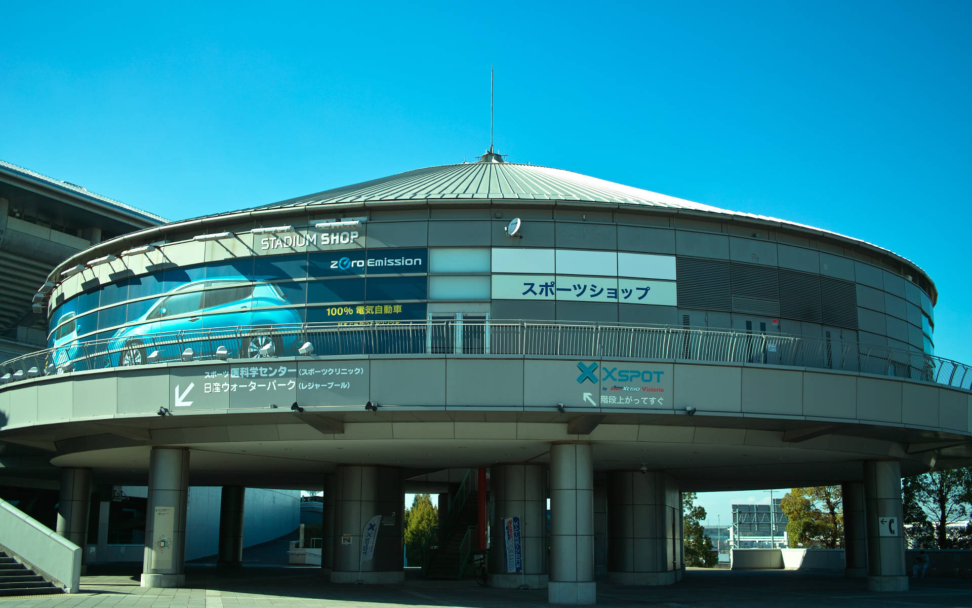橫濱 桌布 壁紙 — 一座現代圓形體育館建築，玻璃幕牆，藍色汽車廣告，在清澈藍天下。