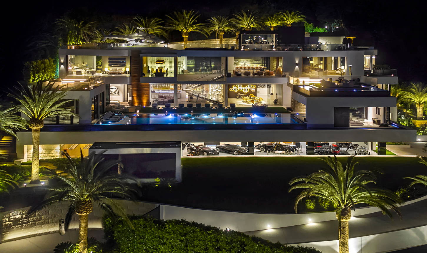 Luxury House 桌布 壁紙 — 一座現代多層豪宅在夜間亮起，內部發光，棕櫚樹和泳池反射藍色燈光。