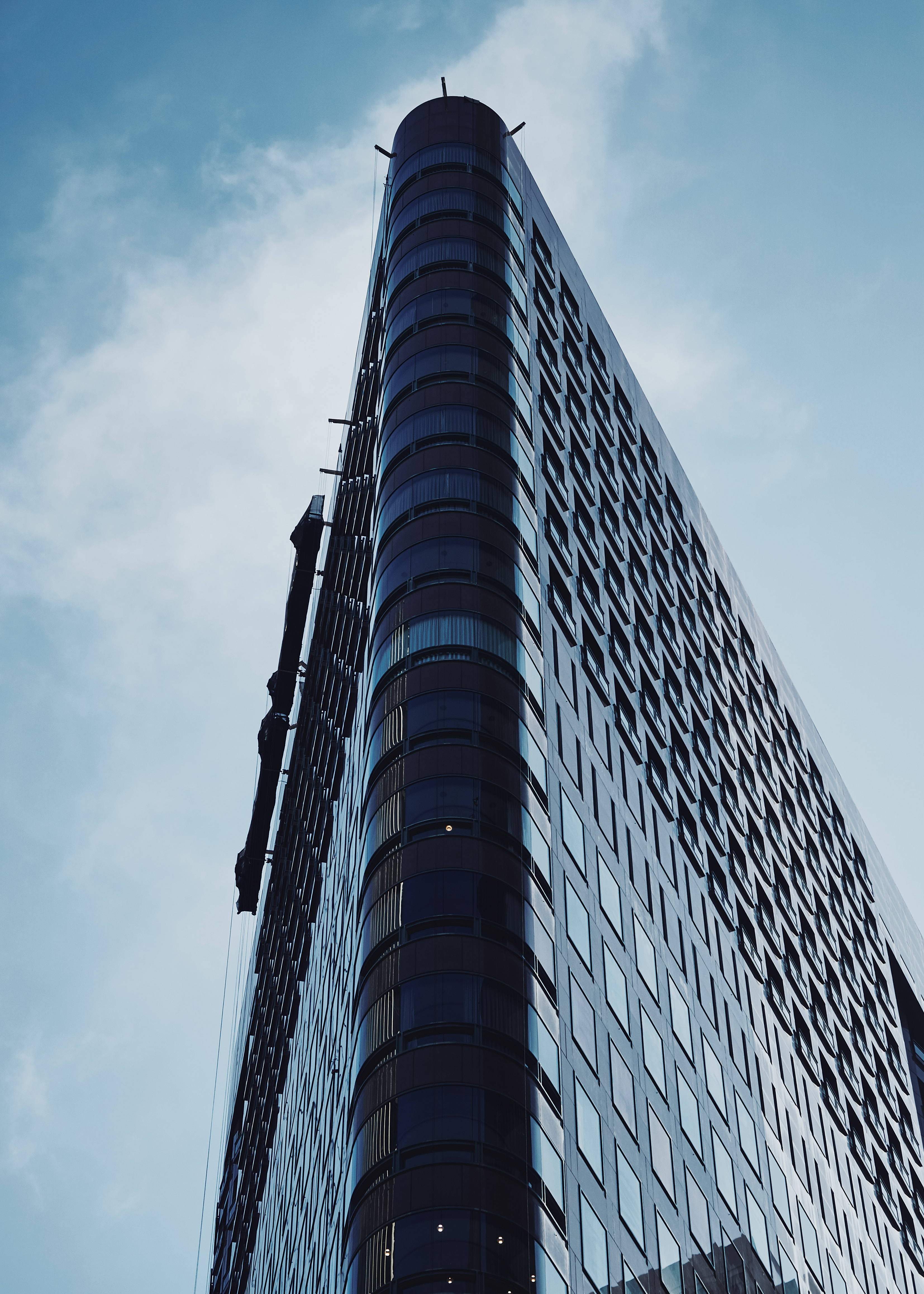 Building 桌布 壁紙 — 一座現代摩天大樓，擁有彎曲的玻璃外牆和幾何圖案，在淺藍色的天空和薄雲中聳立。