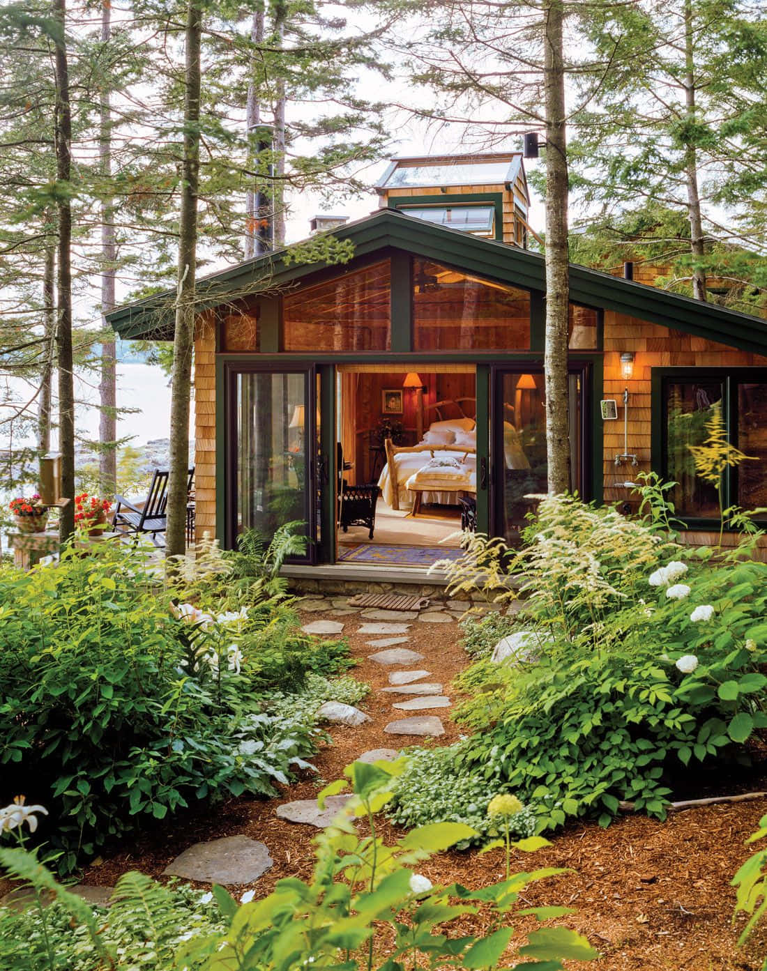 Cottage 桌布 壁紙 — 一座現代木屋坐落在茂密的森林中，石徑通往玻璃門，露出舒適的臥室。